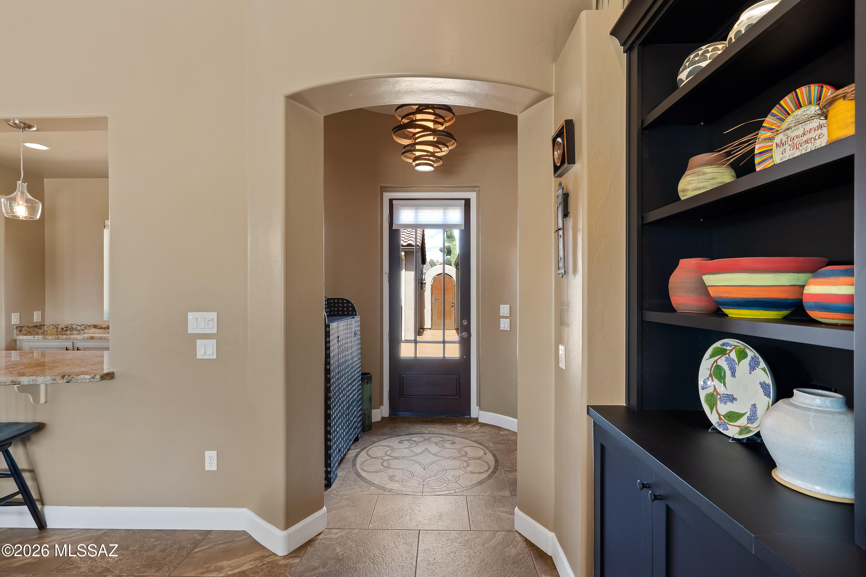 Entry foyer with a circular tile medallion, arched passage, glass-panel door, and colorful pottery on built-in shelves.