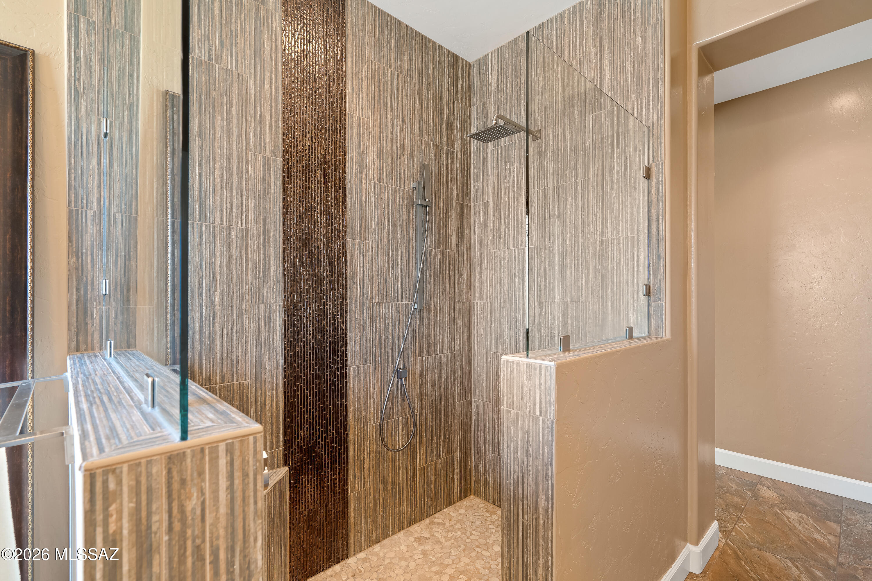 Walk-in shower with frameless glass, rainfall showerhead, dark tile accent, and pebble-stone floor.