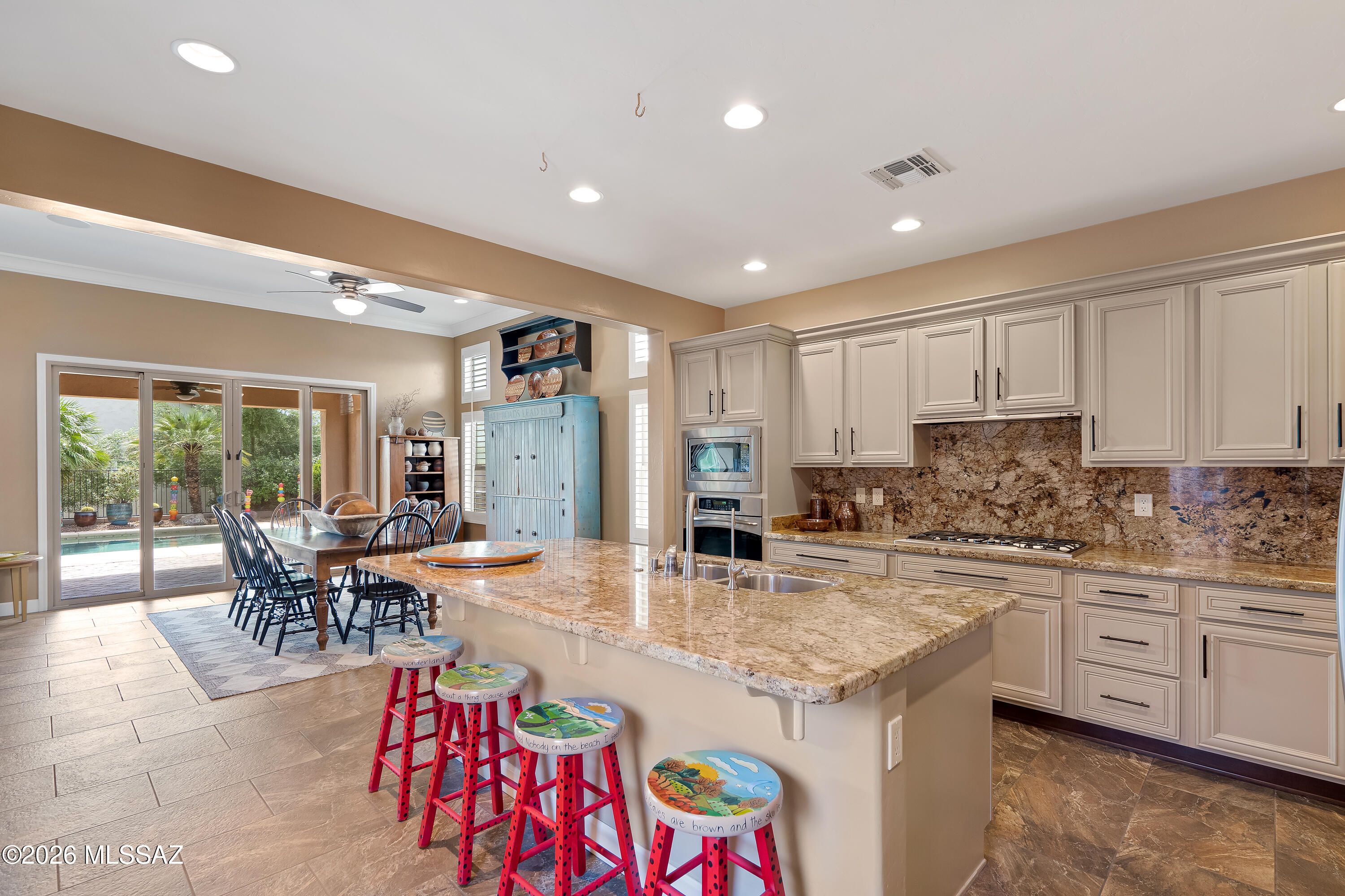 Kitchen with a large stone island, colorful stools, and sliding doors overlooking a pool patio.