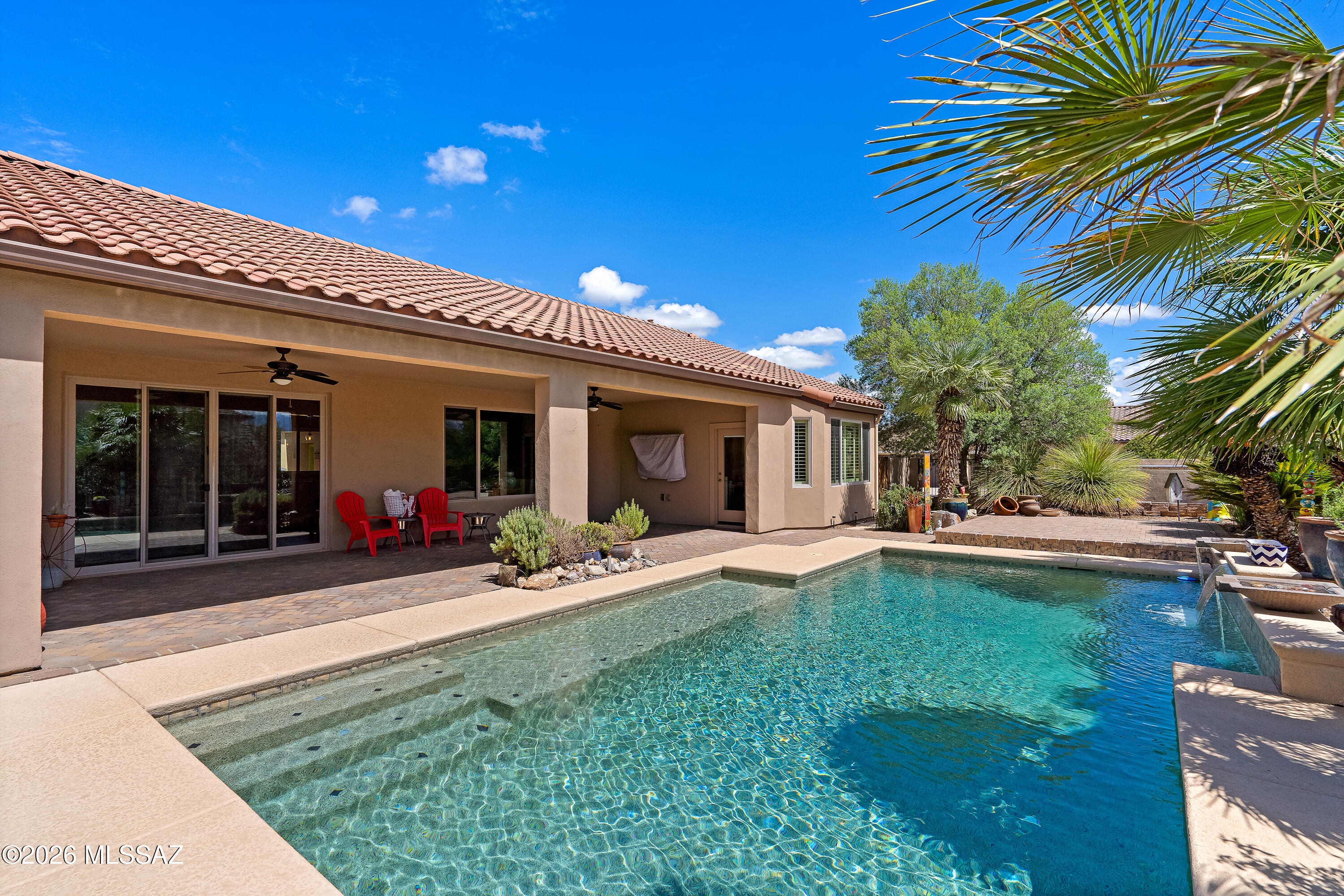 Home’s covered patio and tiled roof overlook a swimming pool framed by palms and desert landscaping.