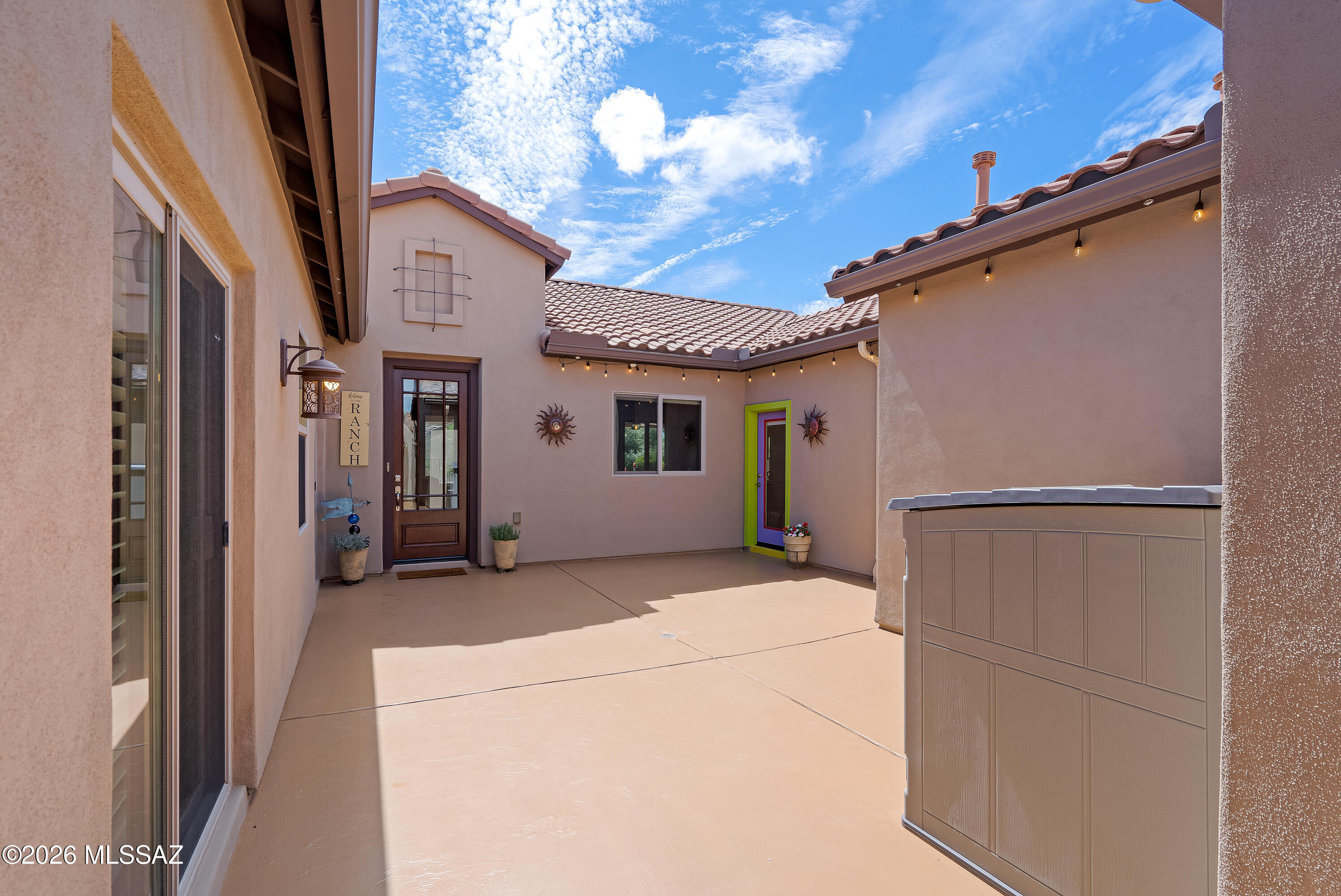 Enclosed stucco courtyard patio with colorful entry doors, string lights, and a covered spa.