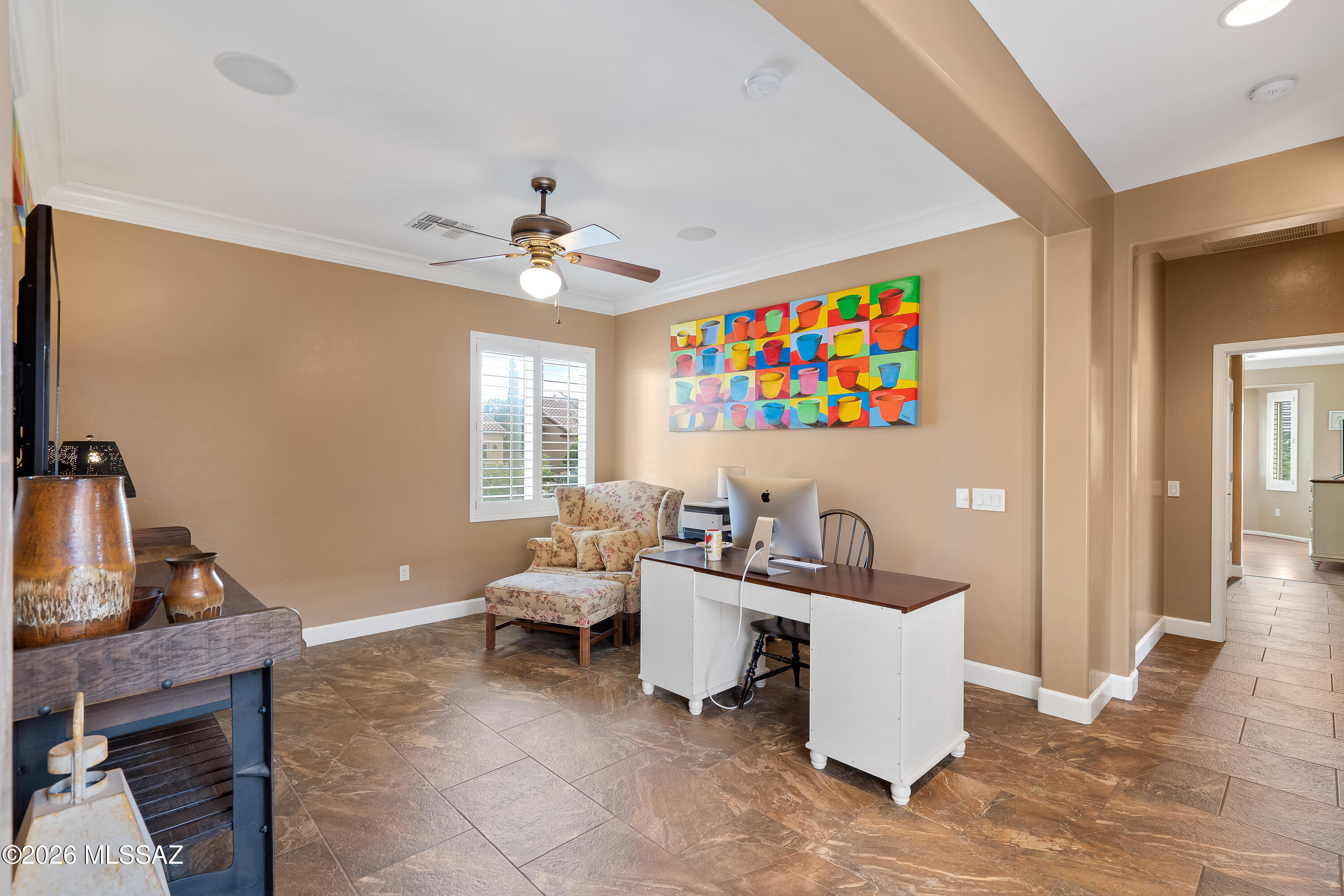 Home office with a white desk and computer, floral chair, and colorful artwork above.