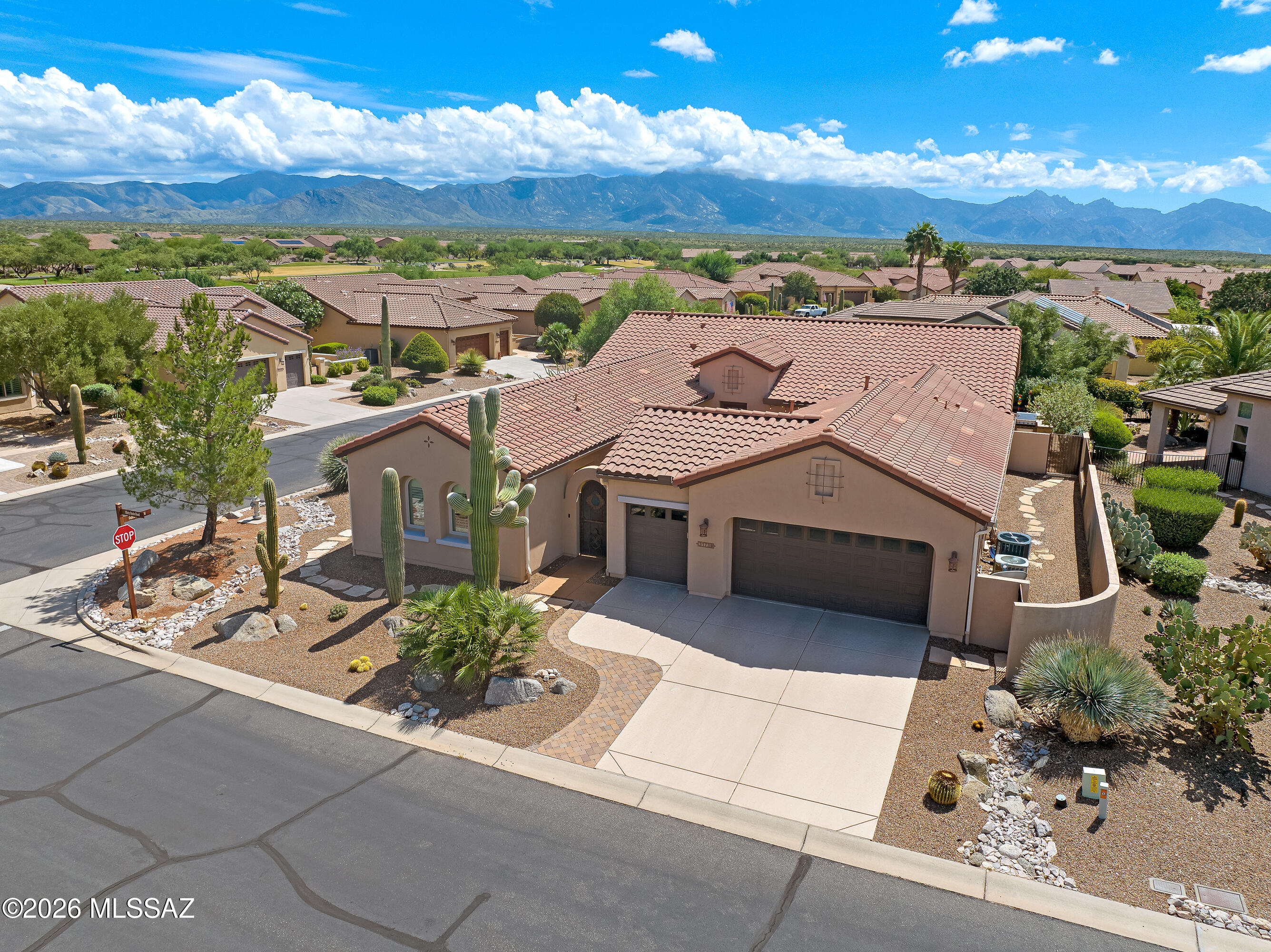 Desert home with a tile roof and cactus landscaping, with mountains rising behind the neighborhood.