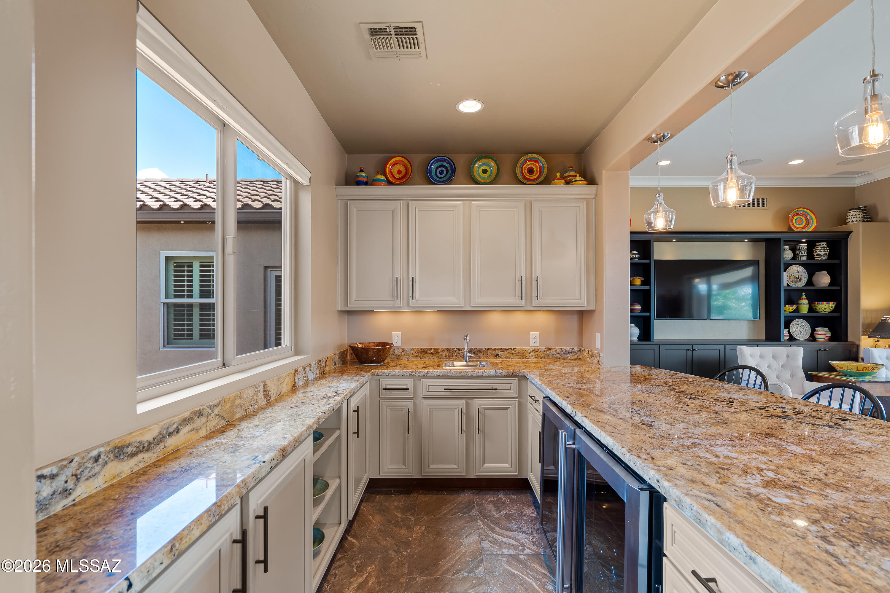 Kitchen with extensive stone countertops, white cabinets, large windows, and colorful pottery.