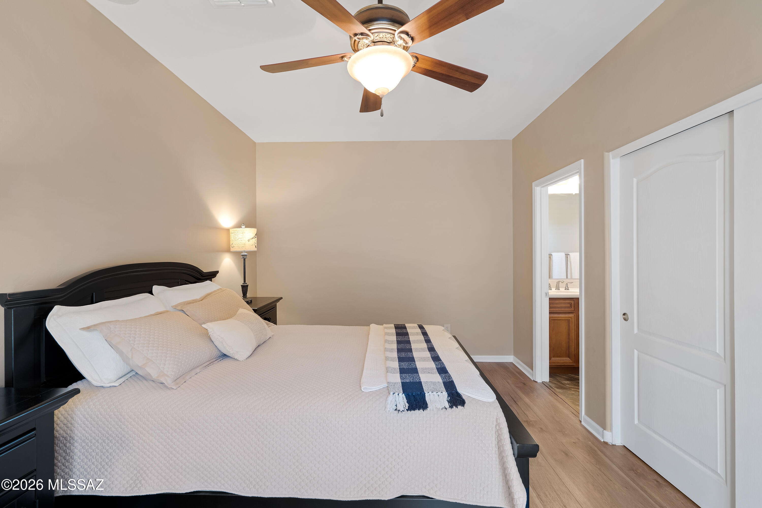 Furnished bedroom with a dark wood headboard, ceiling fan, and doorway to an ensuite bathroom.