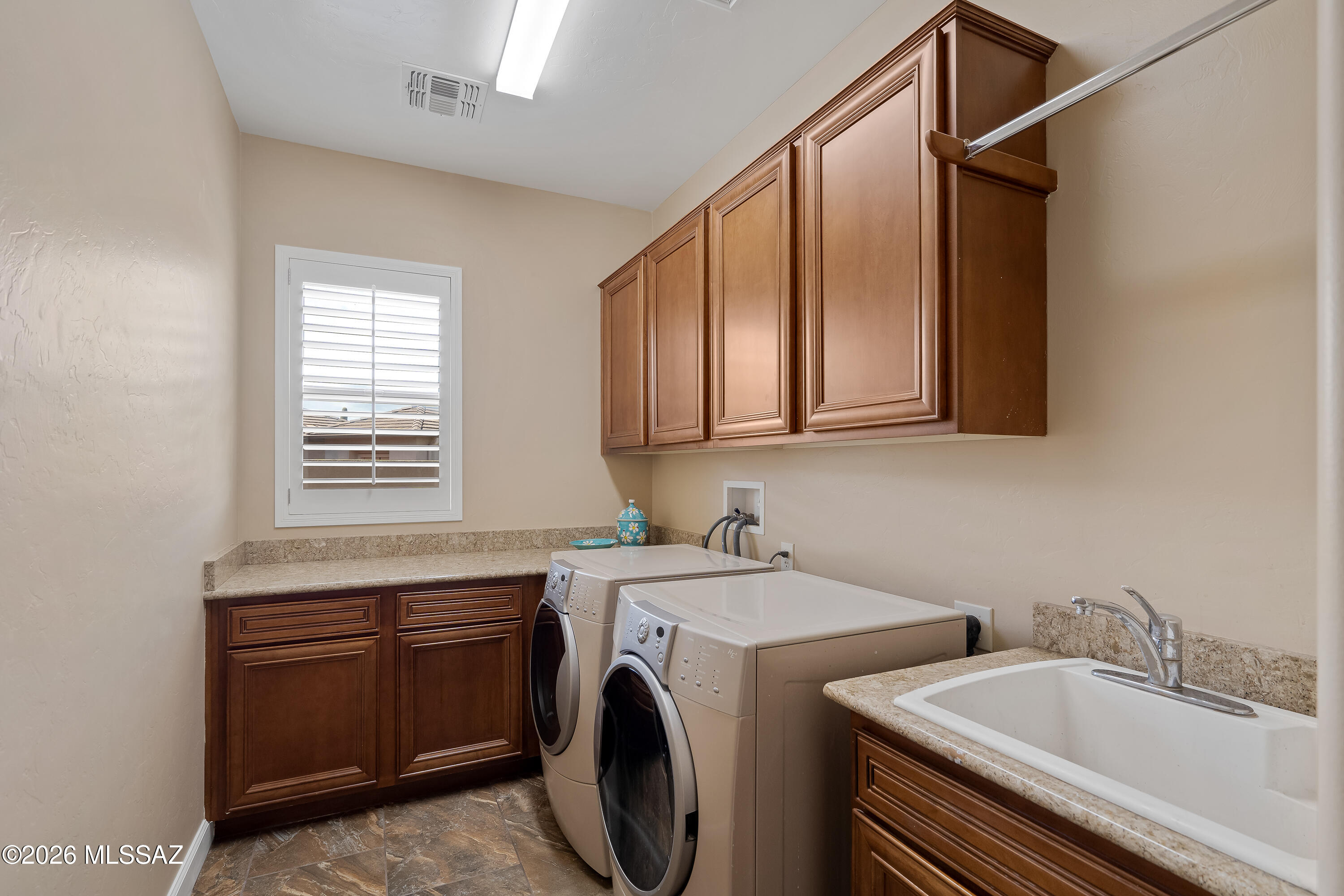 Laundry room with front-loading washer and dryer, deep utility sink, and dark wood cabinetry.