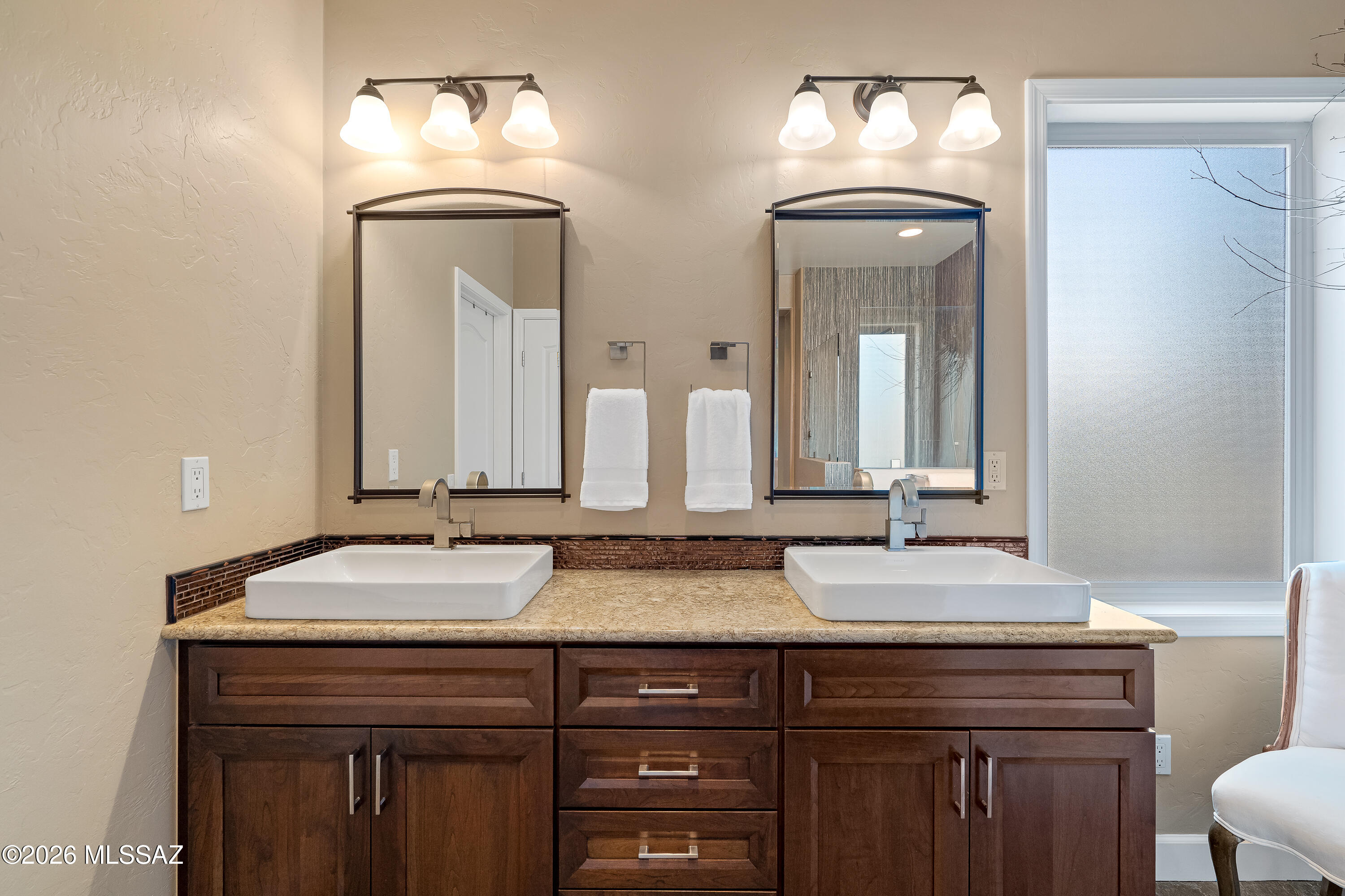 Bathroom double vanity with two vessel sinks, dark wood cabinetry, matching mirrors, and a frosted window.