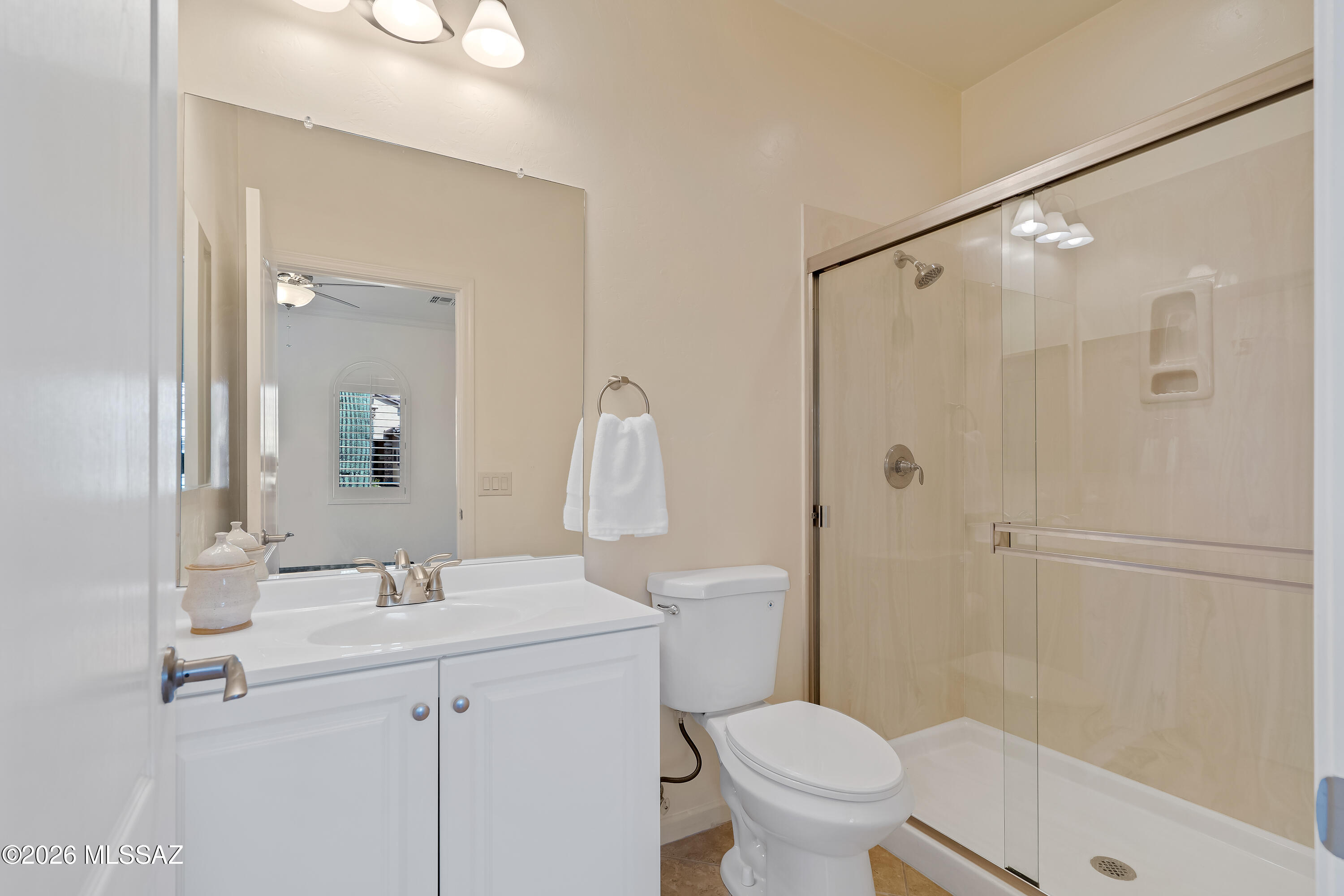 Bathroom with a white vanity, toilet, and glass-enclosed beige-tile shower.