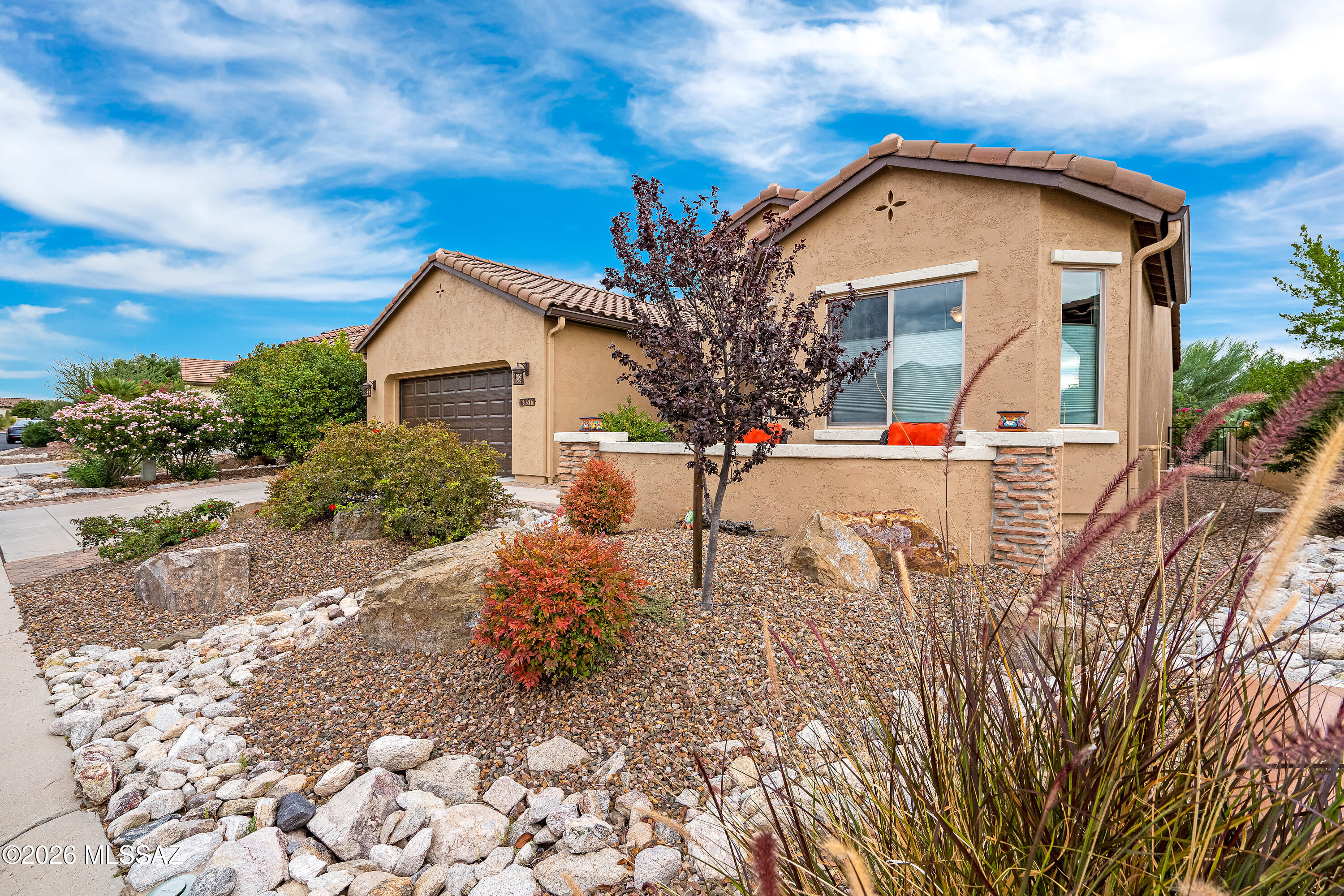 Tan stucco home with attached garage, tile roof, and desert rock landscaping.