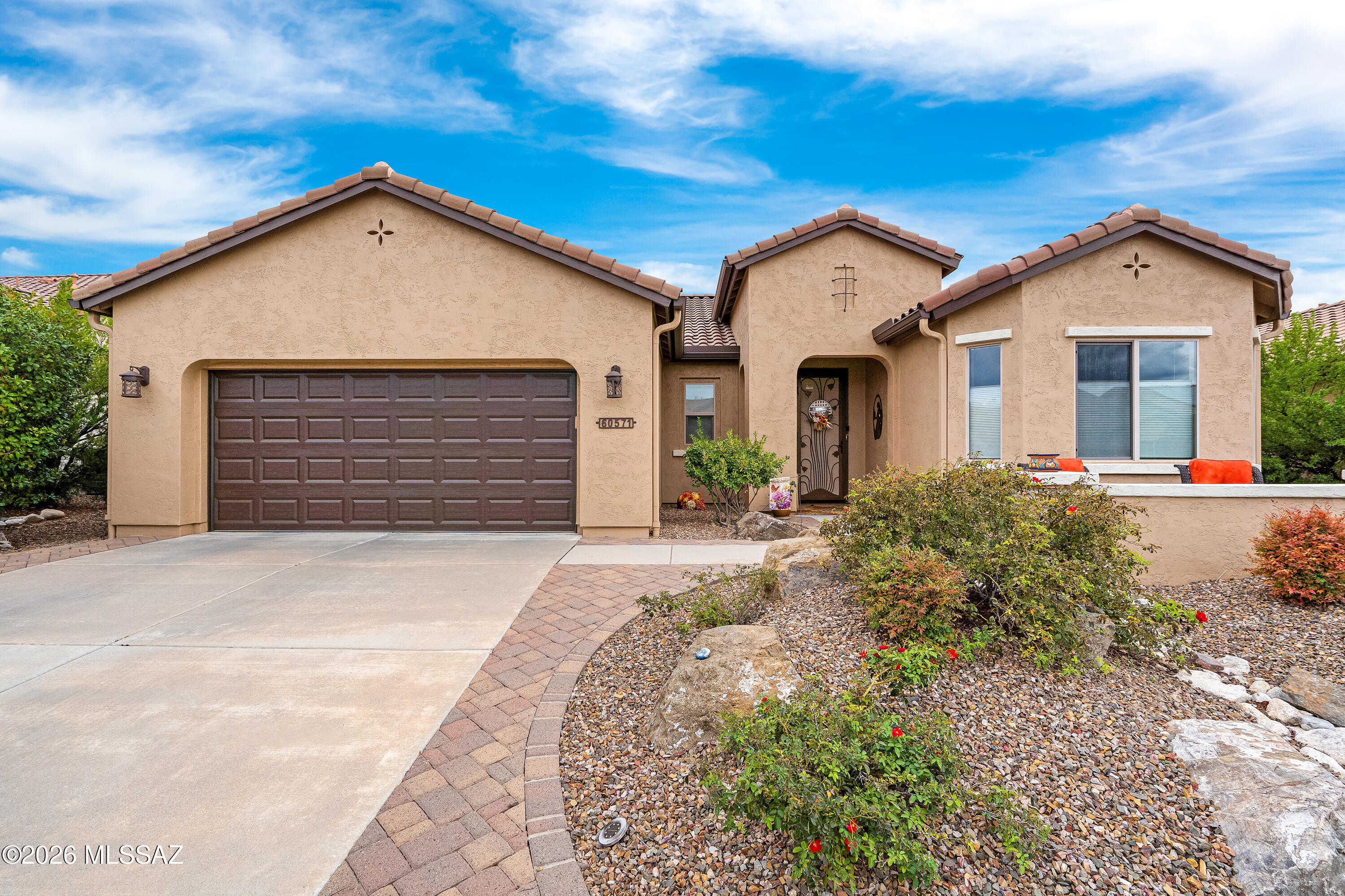 Tan stucco home with a tiled roof, two-car garage, and rock landscaping.
