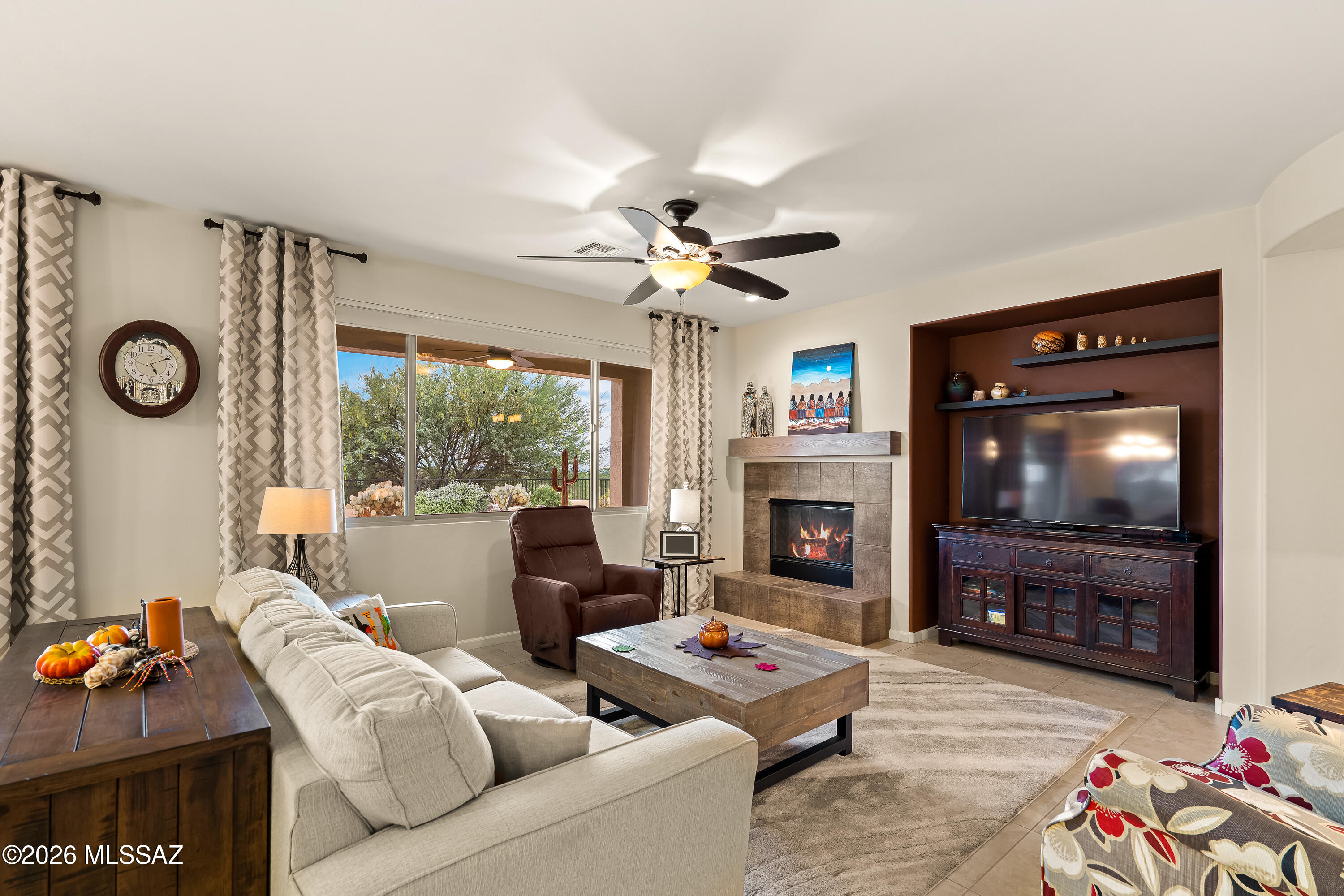 Living room with a stone fireplace, built-in TV alcove, and large window overlooking desert landscaping.