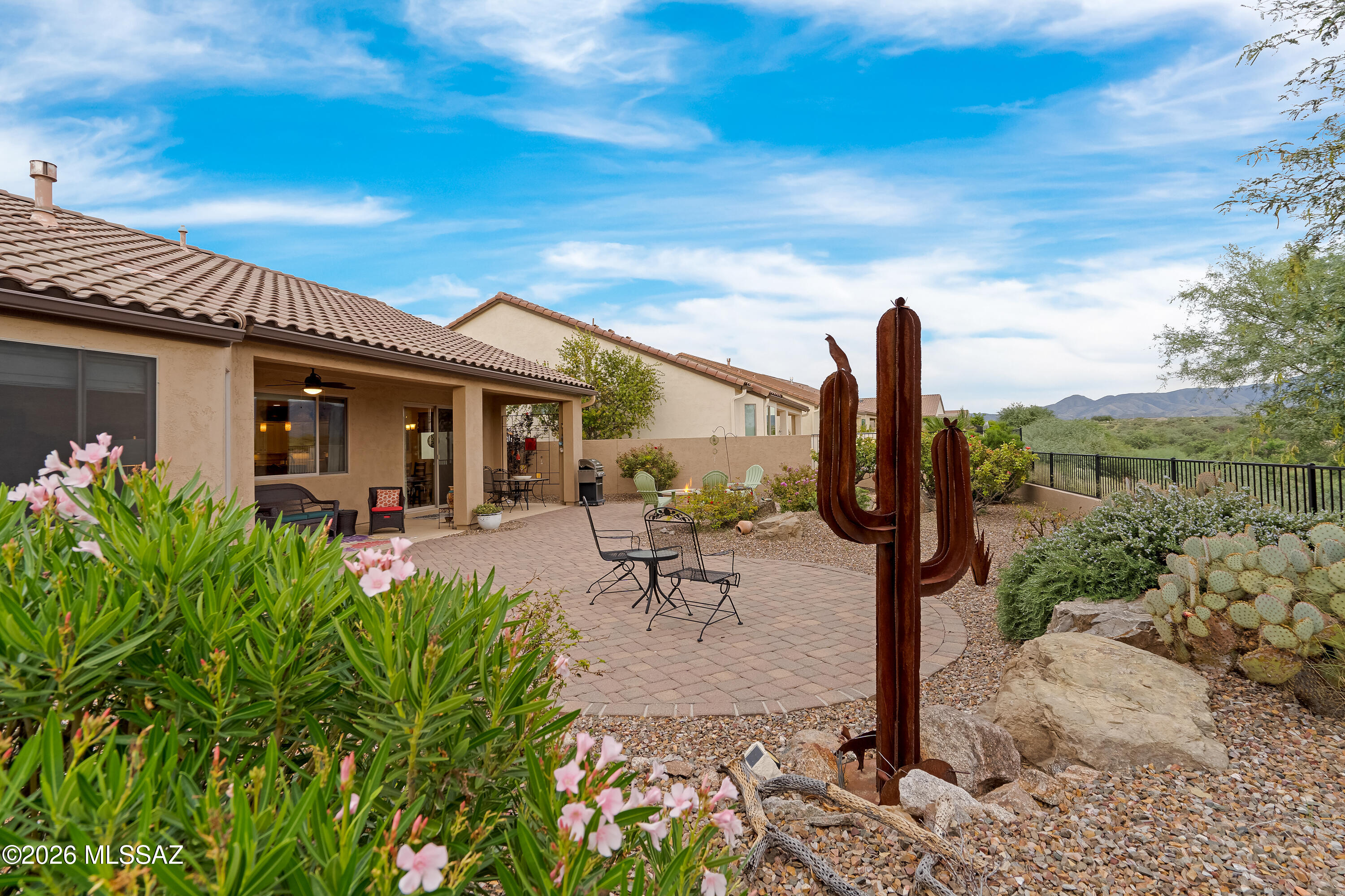 Covered patio with outdoor seating, desert landscaping, a saguaro sculpture, and distant mountains.