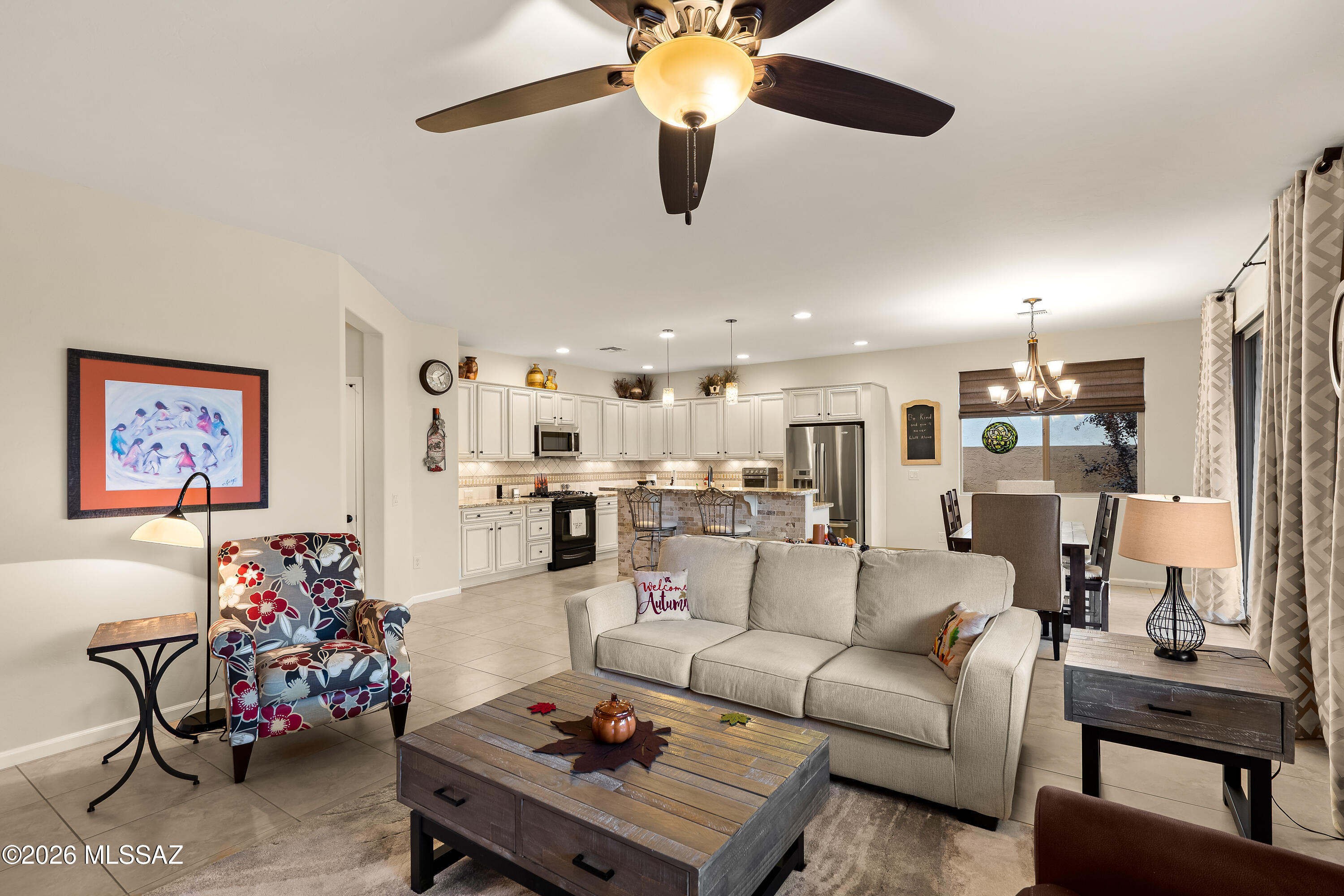 Open-plan living room with cream sofa, colorful armchair, and adjoining white kitchen and dining area.