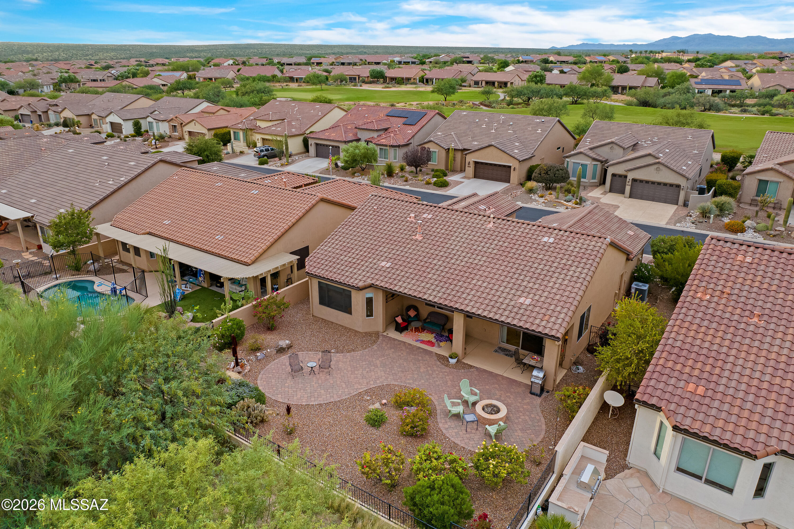 Aerial view of a tiled-roof home with a paved backyard patio, fire pit, and mountain backdrop.