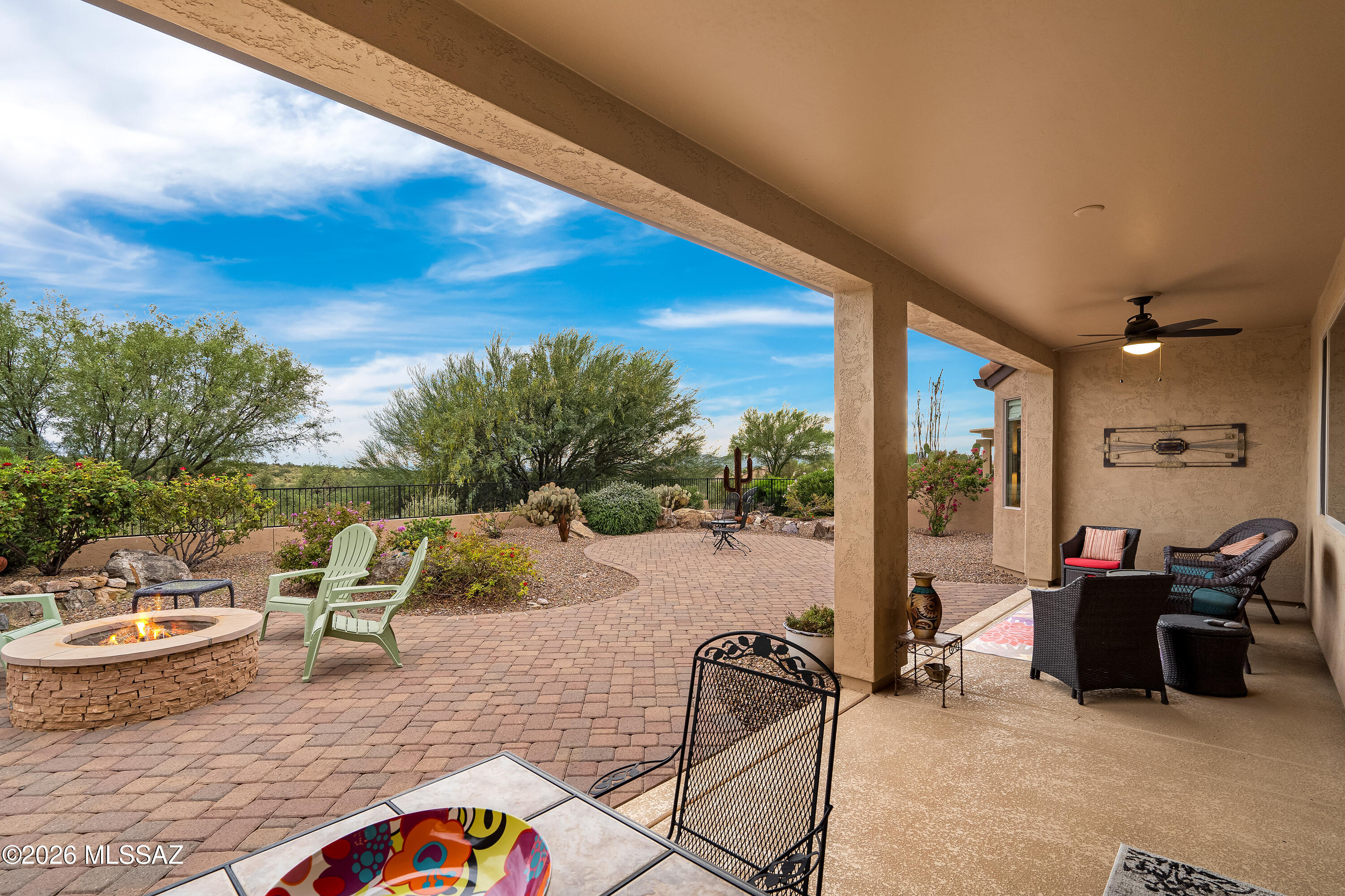 Covered patio and paver courtyard with a fire pit, outdoor seating, and desert landscaping.