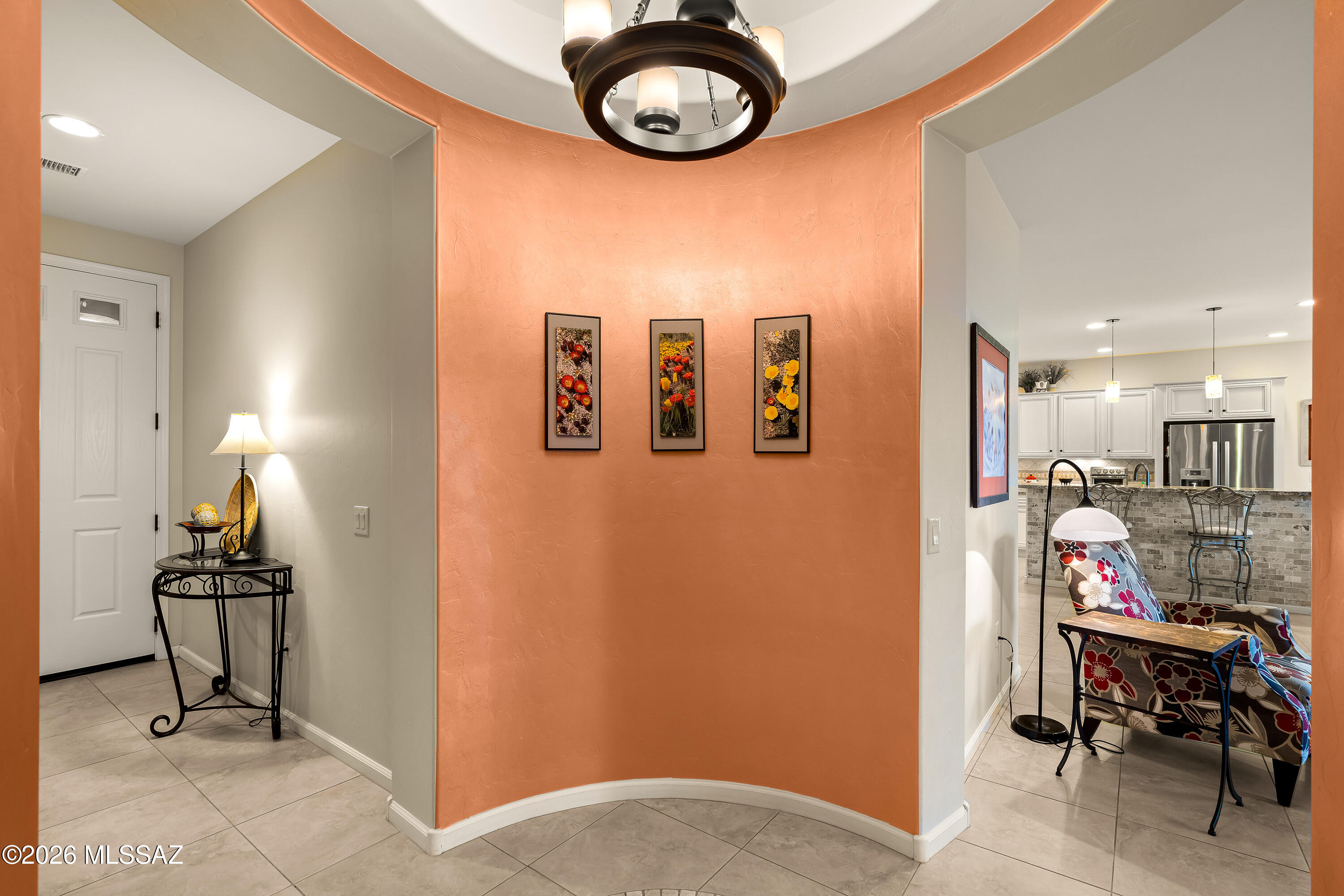 Entry foyer with a curved terracotta wall, floral prints, and a view into the kitchen and sitting area.