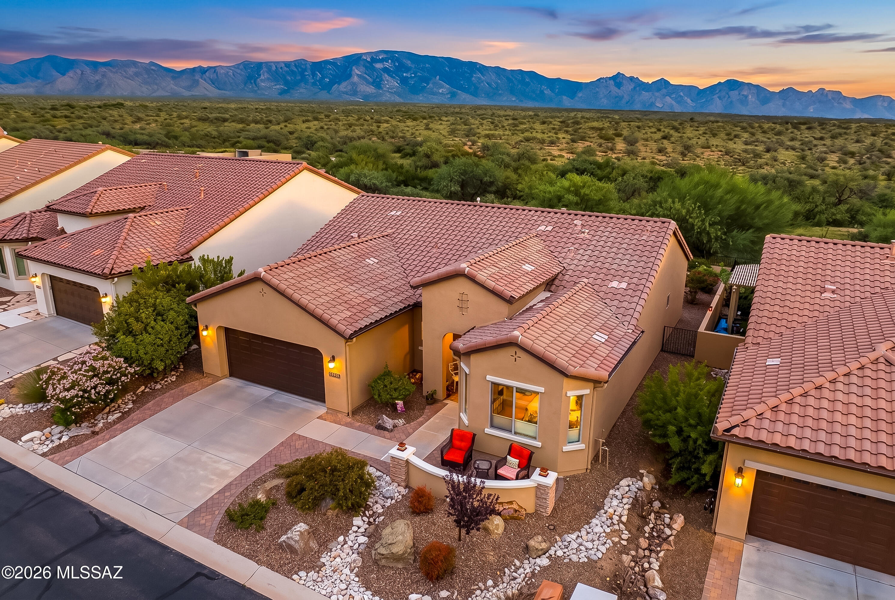 Aerial view of a desert home with a red tile roof, landscaped yard, and mountains at dusk.