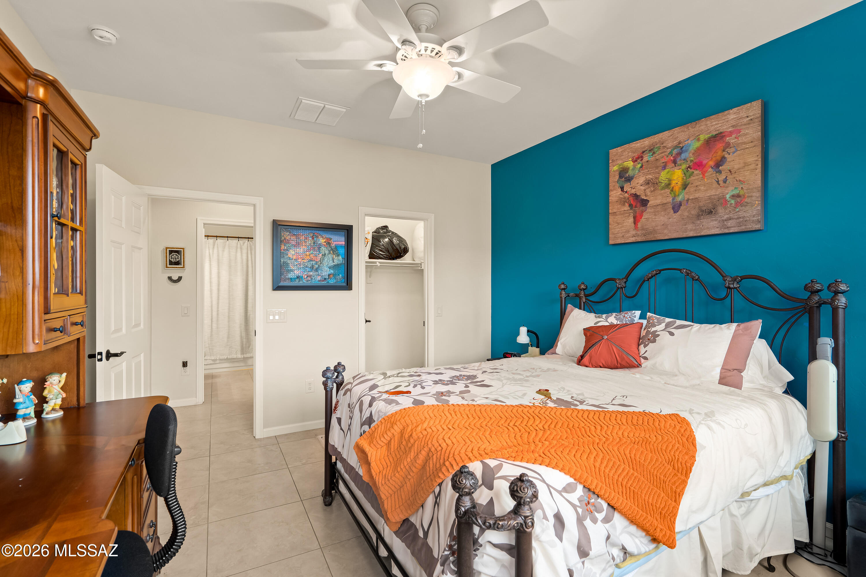 Bedroom with a wrought-iron bed, orange throw, and teal accent wall with world map artwork.