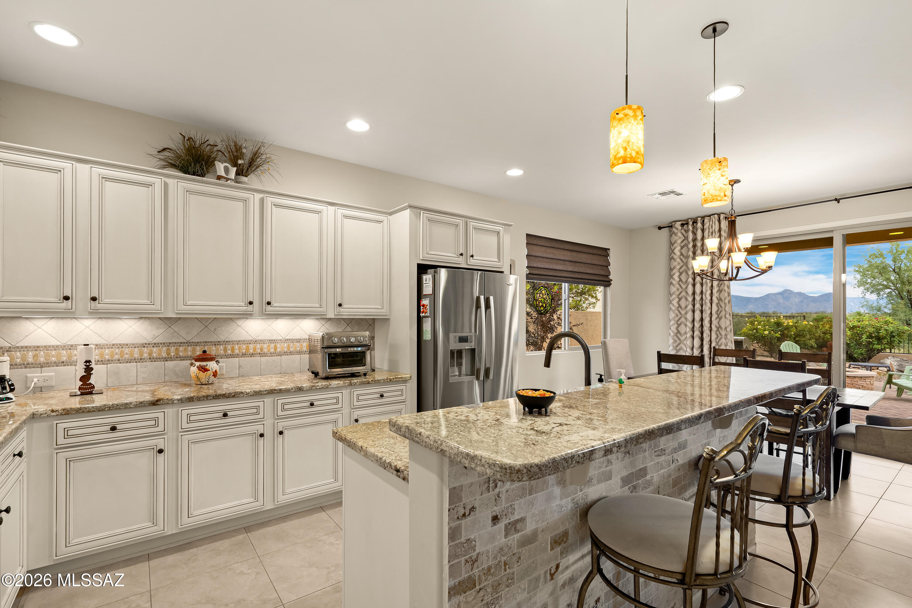 Kitchen with white cabinets, a granite island and bar seating, opening to a patio with mountain views.