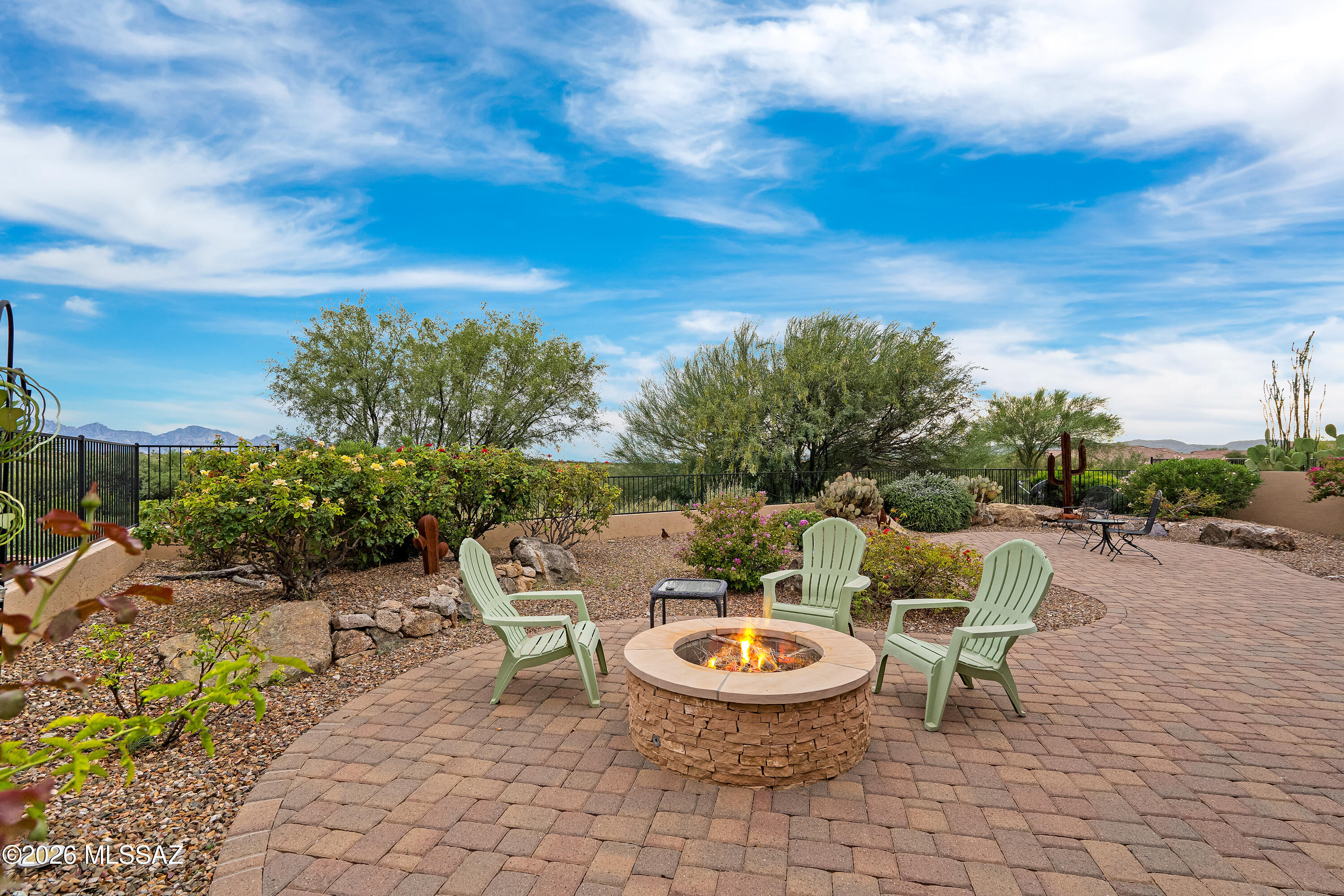 Desert backyard patio with a stone fire pit, Adirondack chairs, desert landscaping, and distant mountains.