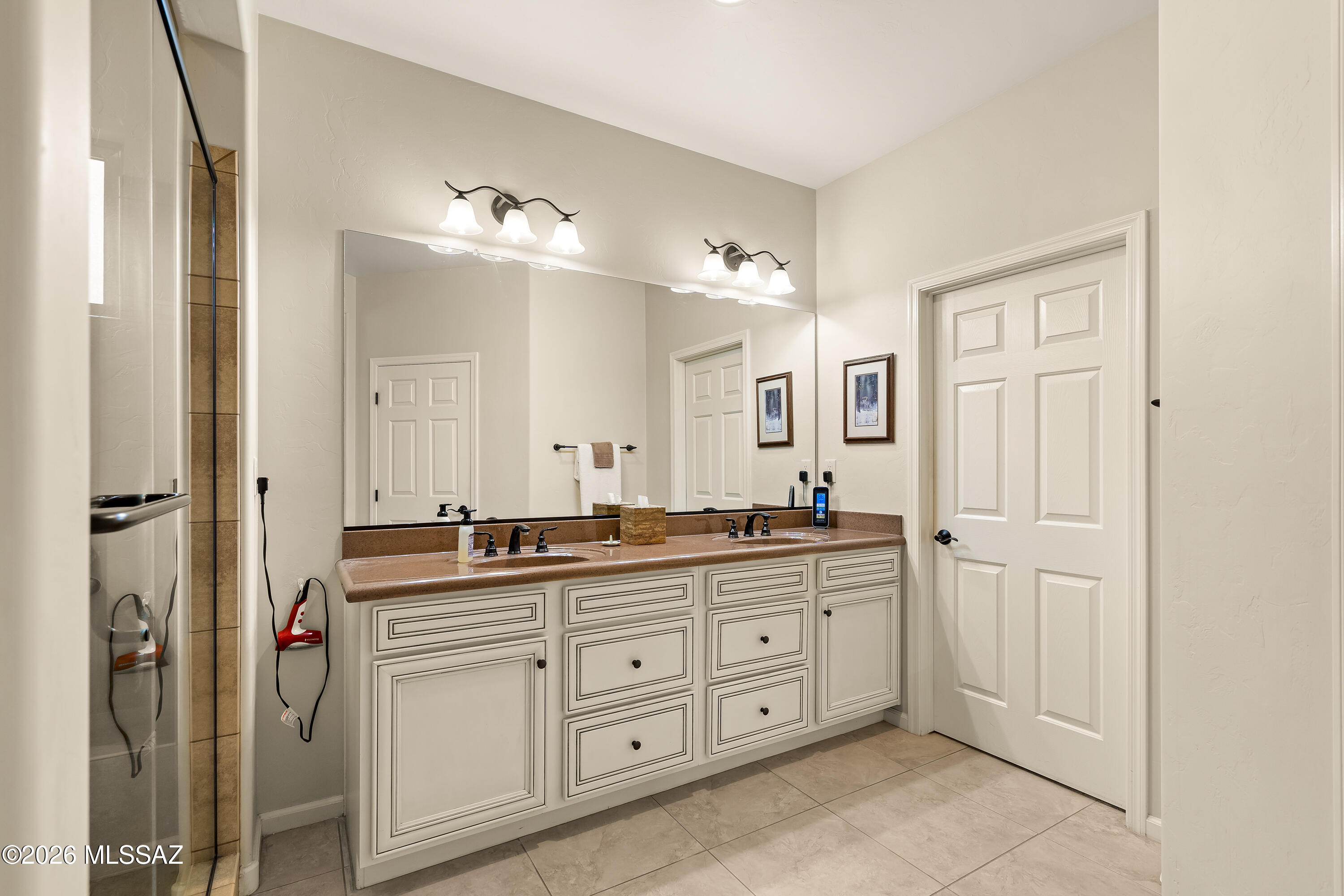 Bathroom with a double-sink vanity, cream cabinets, large mirror, and glass shower.