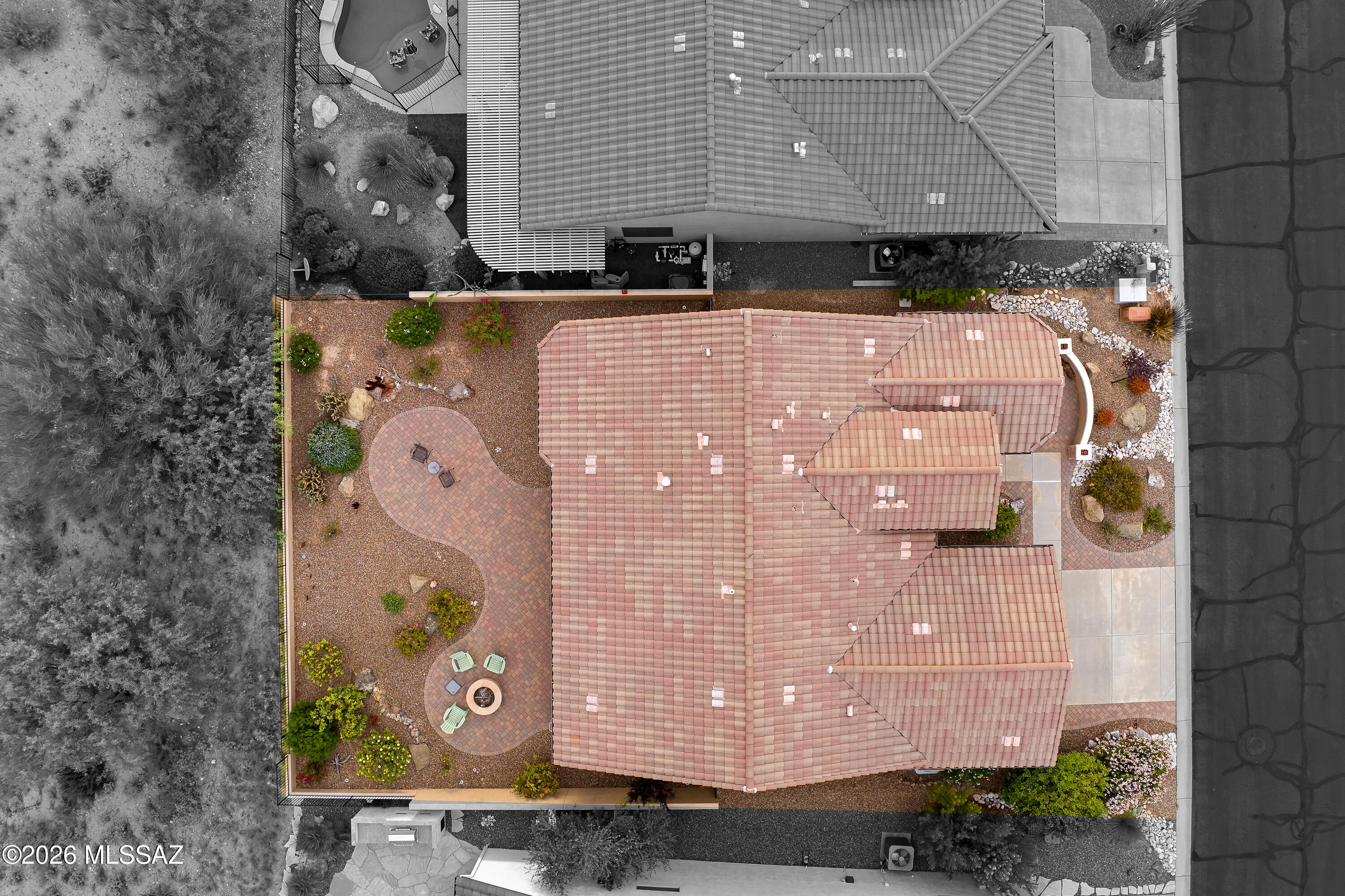 Aerial view of a tile-roofed home with desert landscaping and a curved patio with a fire pit.