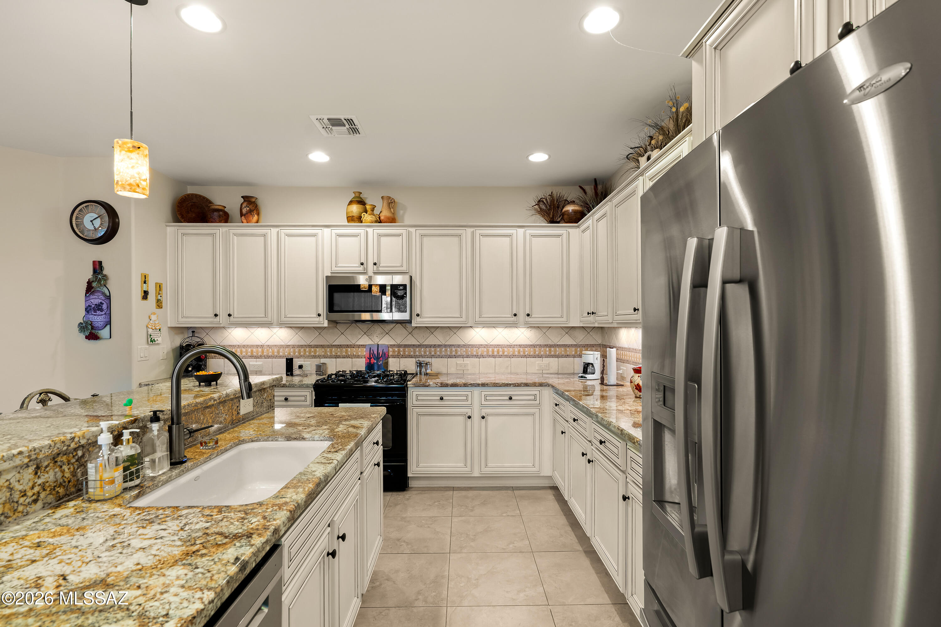 Kitchen with cream cabinets, granite counters, peninsula sink, and large stainless steel refrigerator.