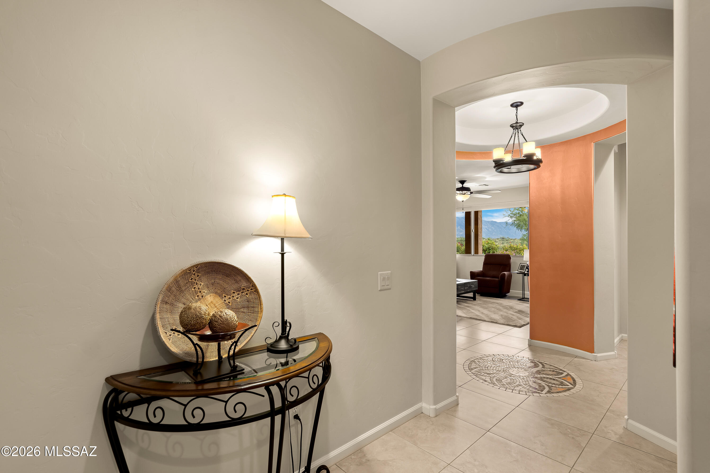 Furnished entryway with a curved console table and lamp, opening to a living room with an orange accent wall and mountain views.