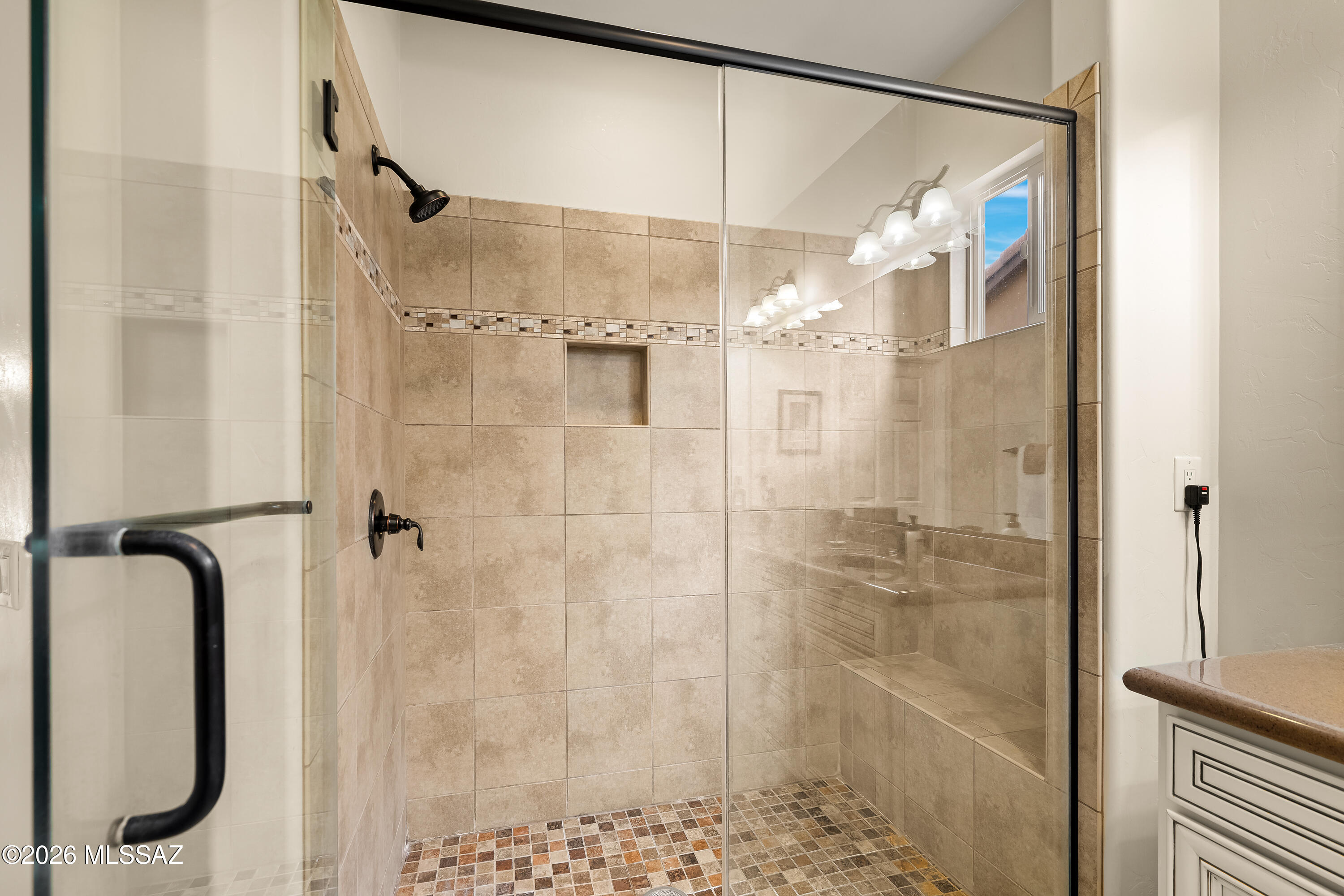 Walk-in shower with clear glass enclosure, beige tile, built-in bench, and mosaic floor.
