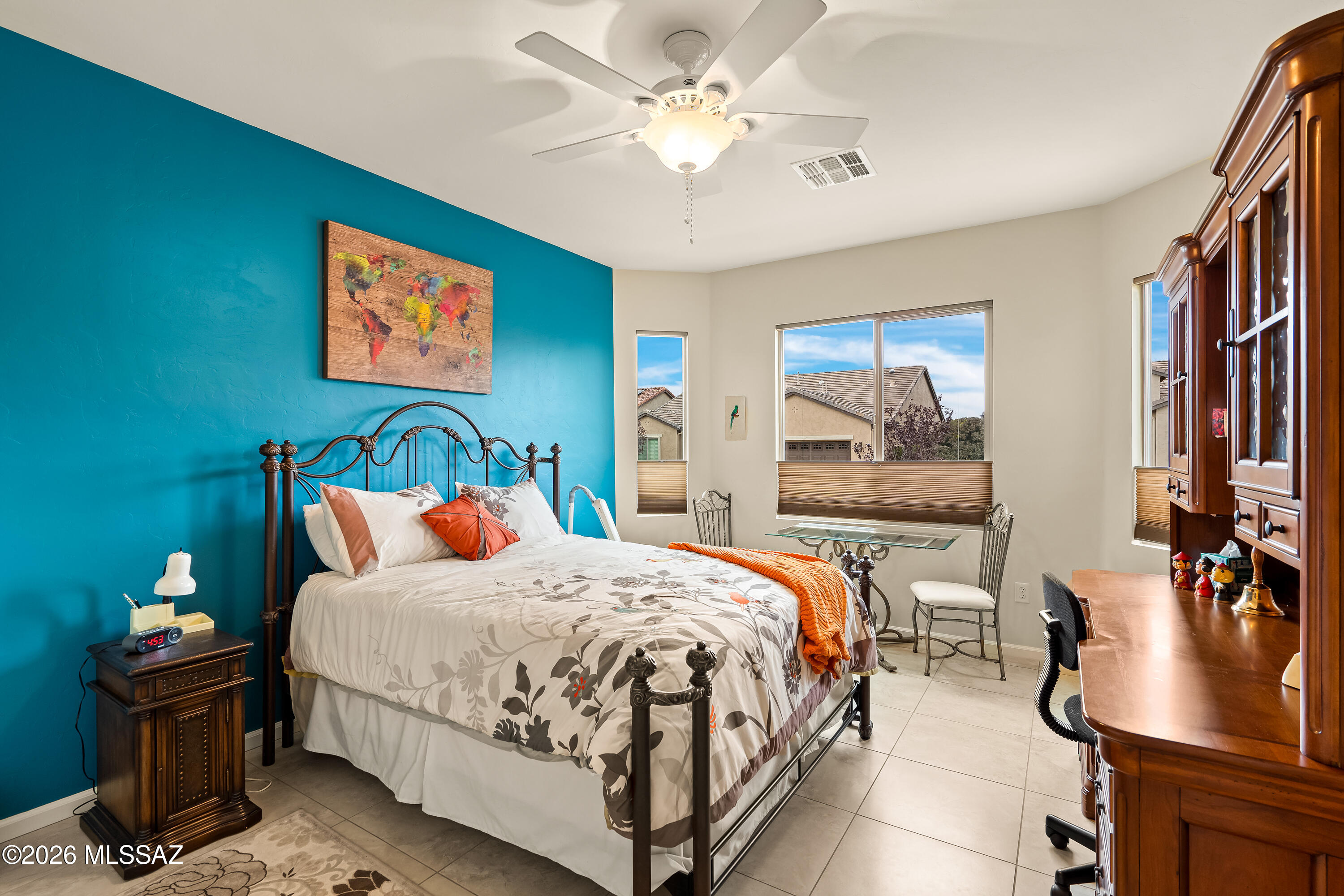 Bedroom with a teal accent wall, black metal bed, orange throw, and wooden desk and cabinets.