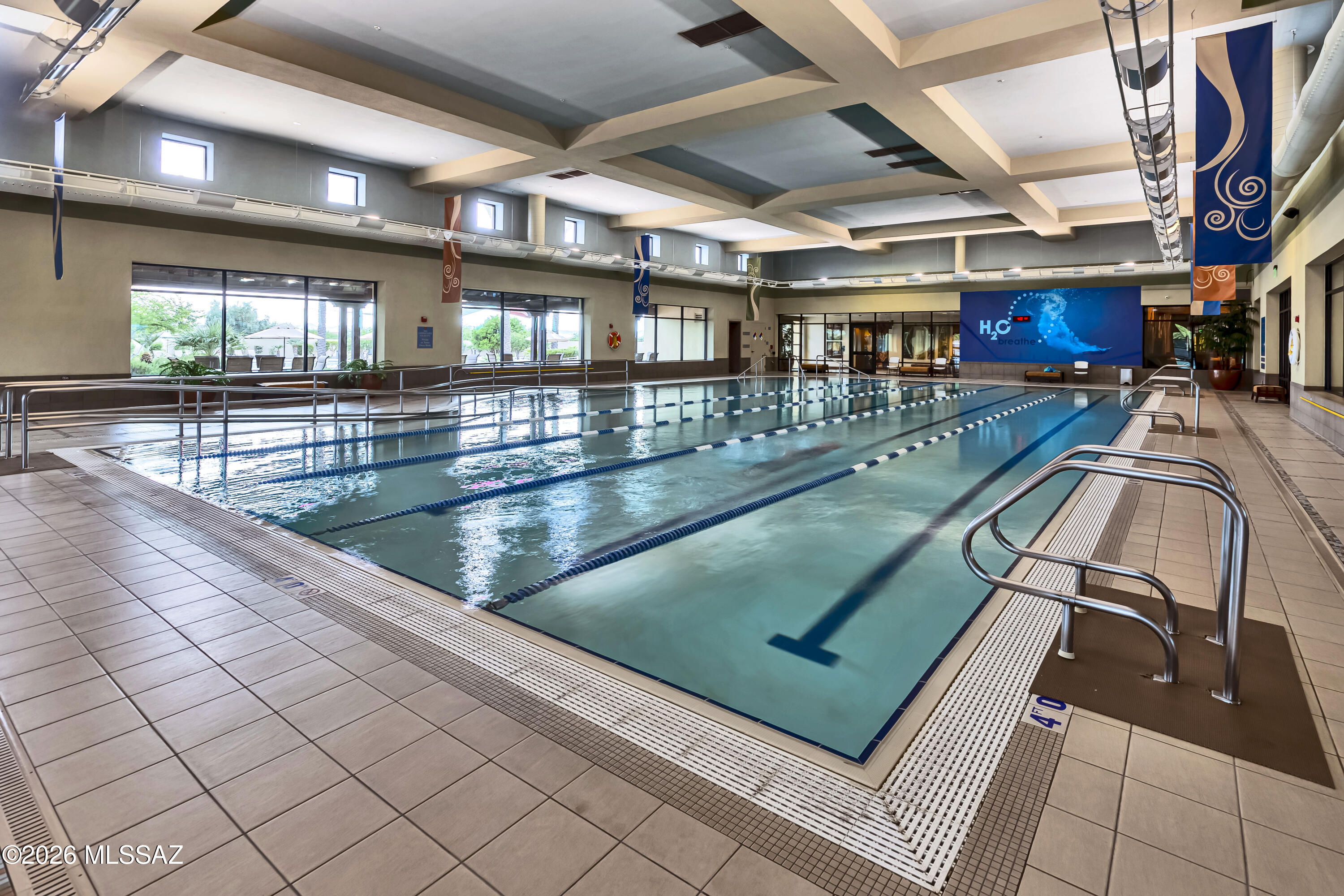 Indoor lap pool with multiple lanes, tiled deck, and metal handrails.
