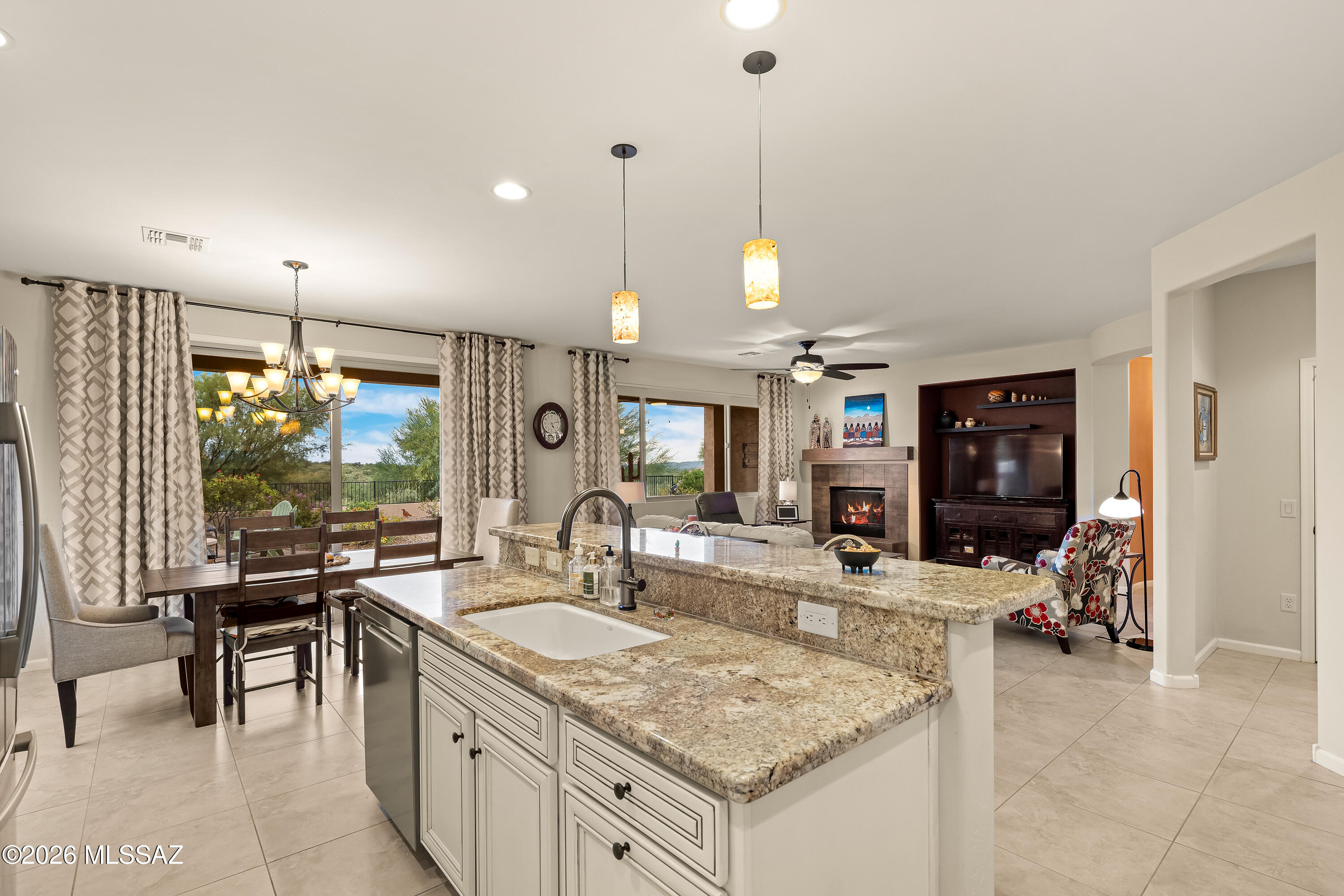 Open kitchen with granite island overlooking dining and living areas, fireplace, and patio.