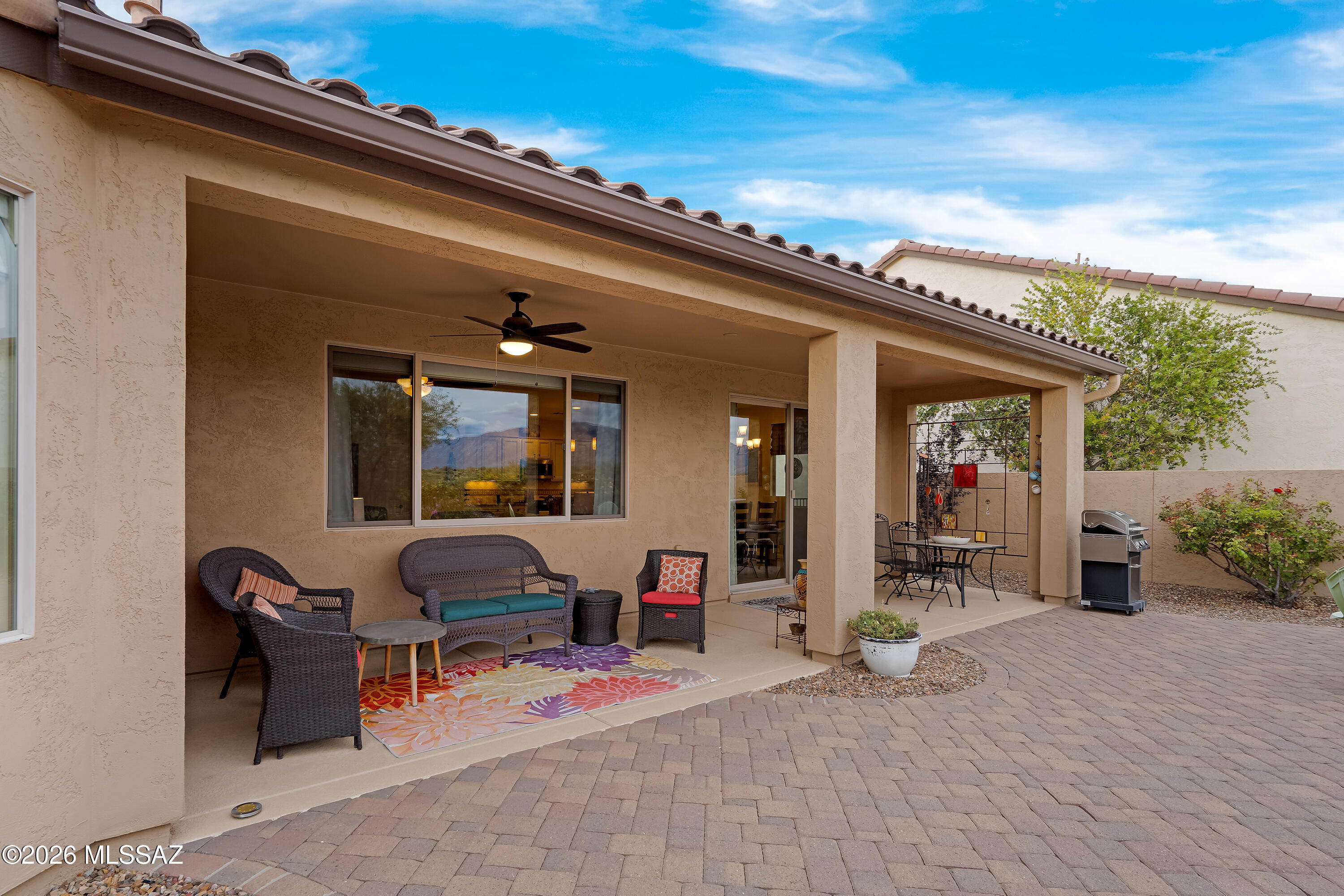Covered patio with wicker seating, colorful rug, ceiling fan, dining table, and barbecue grill.