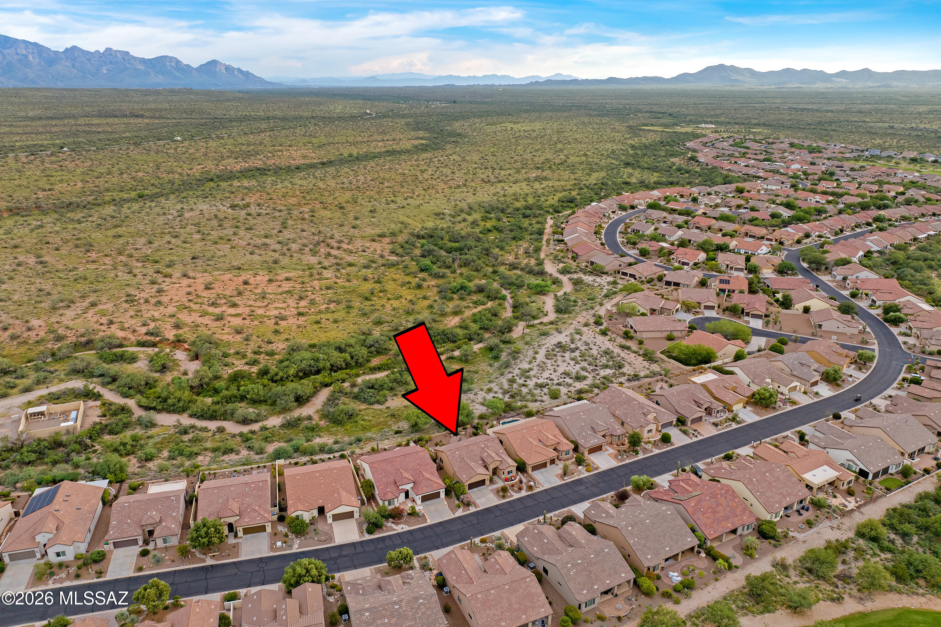 Aerial view of a red-arrow-marked home beside desert with mountains beyond.