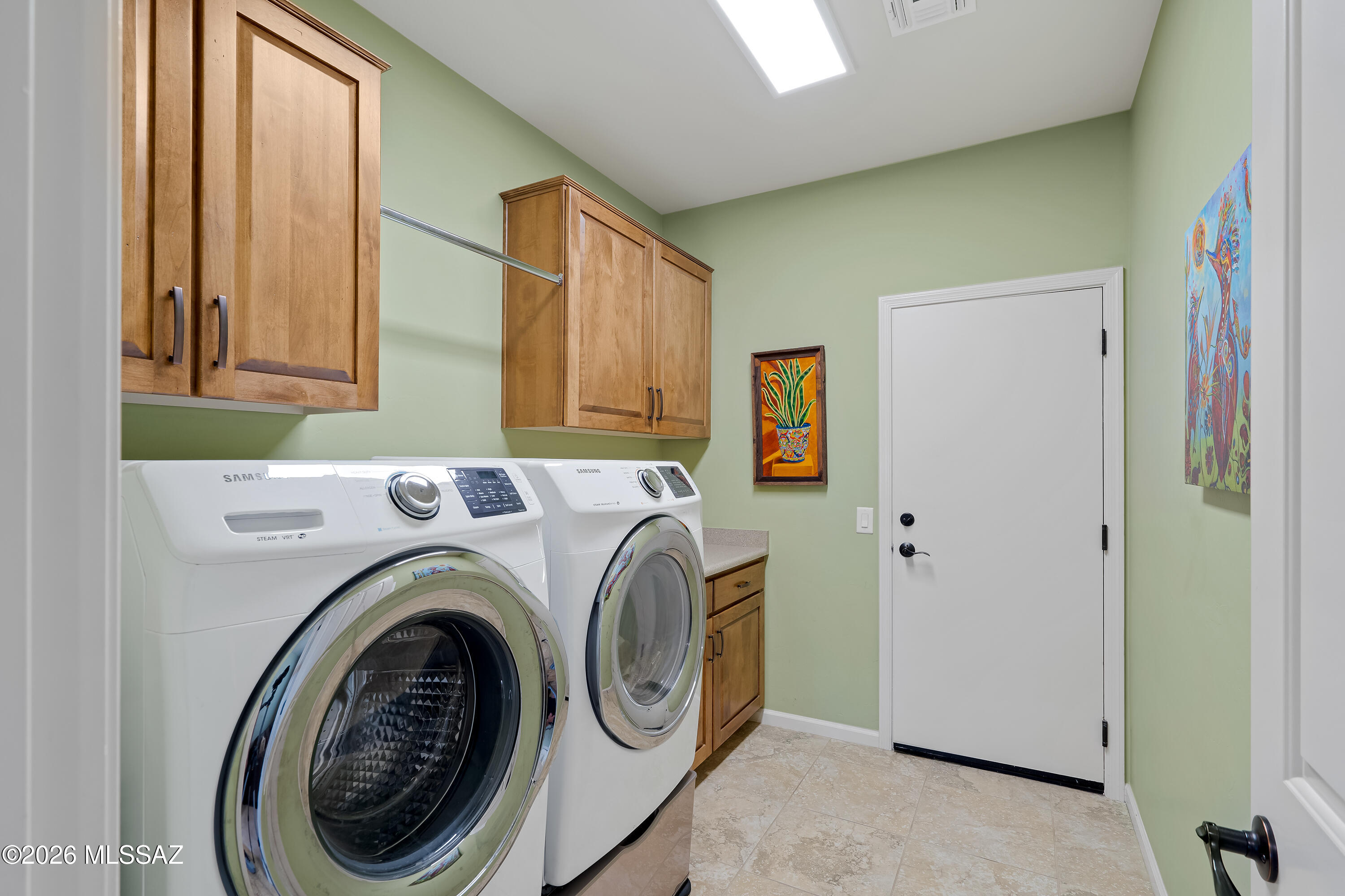 Laundry room with front-loading washer and dryer, wood cabinets, and pale green walls.
