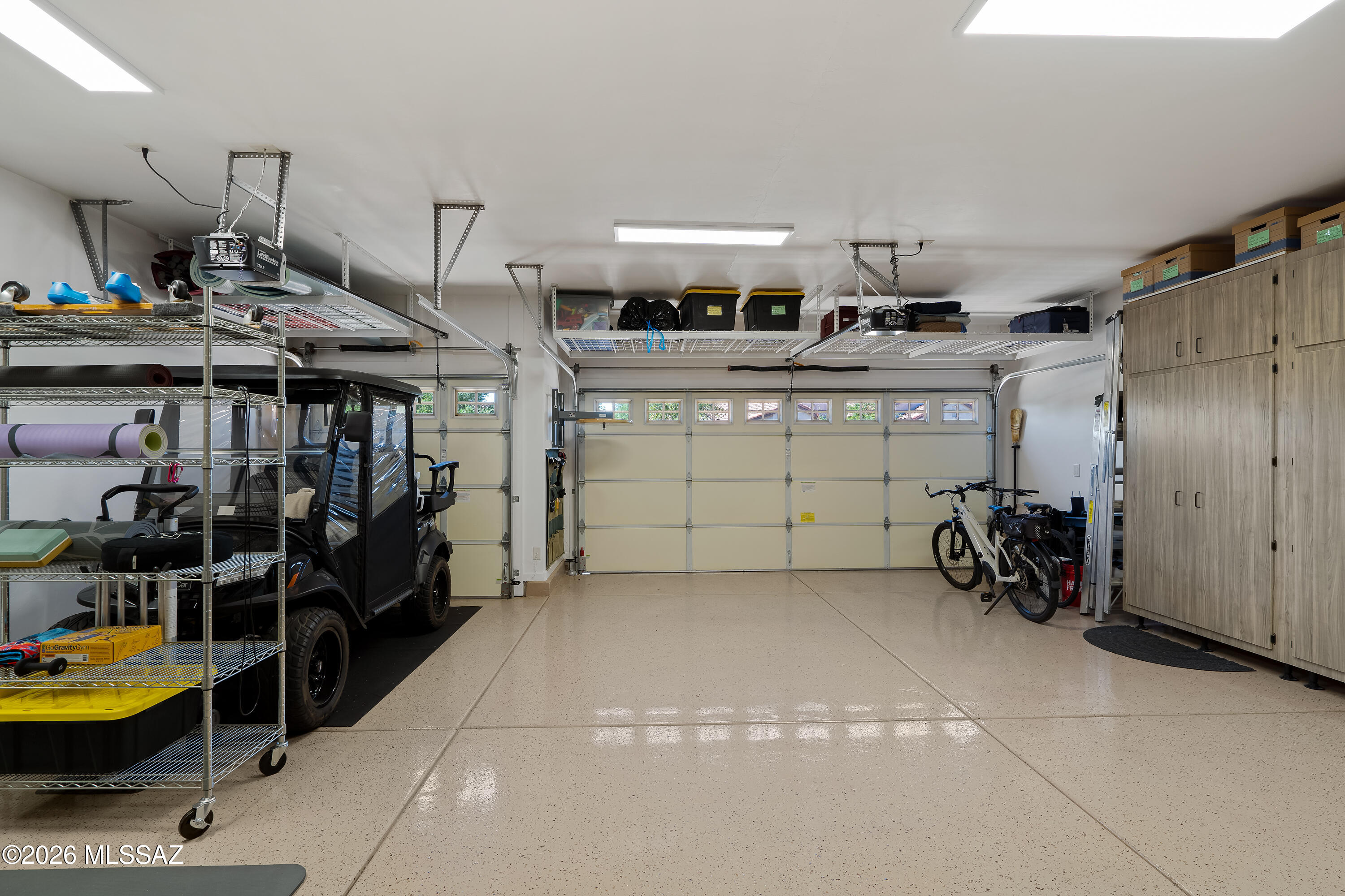 Organized garage with overhead storage racks, tall cabinets, a utility vehicle, and bicycles.