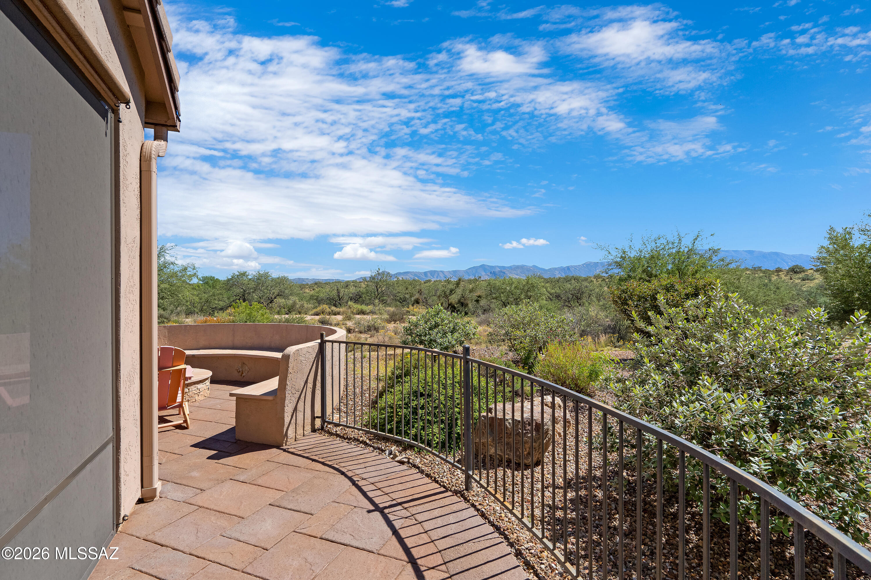Patio with curved stucco seating and metal railing overlooking desert vegetation and distant mountains.