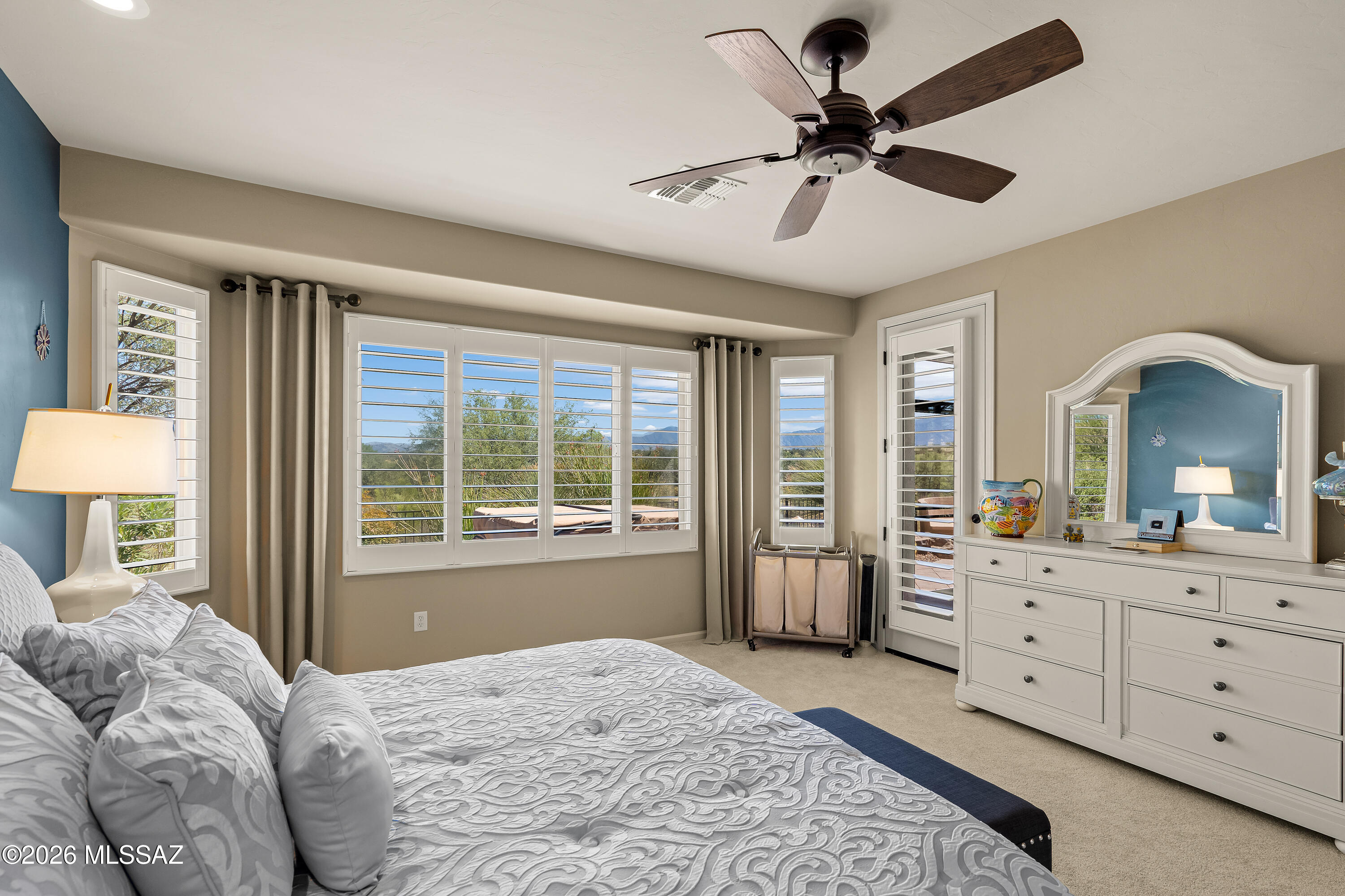 Bedroom with white bedding, a mirrored dresser, and shuttered windows overlooking distant mountains.