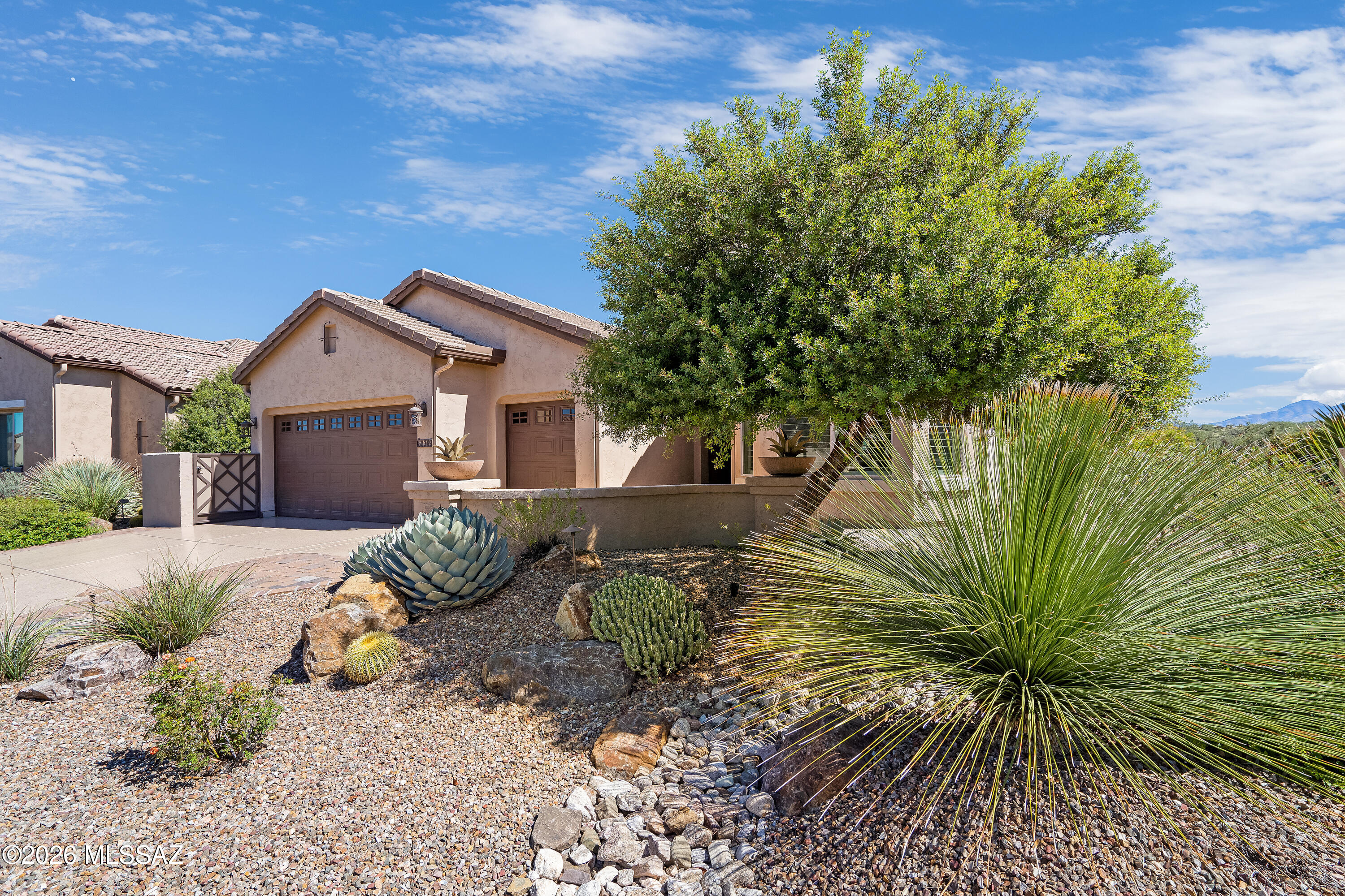 Tan stucco home with two garage doors, desert landscaping, and distant mountain views.