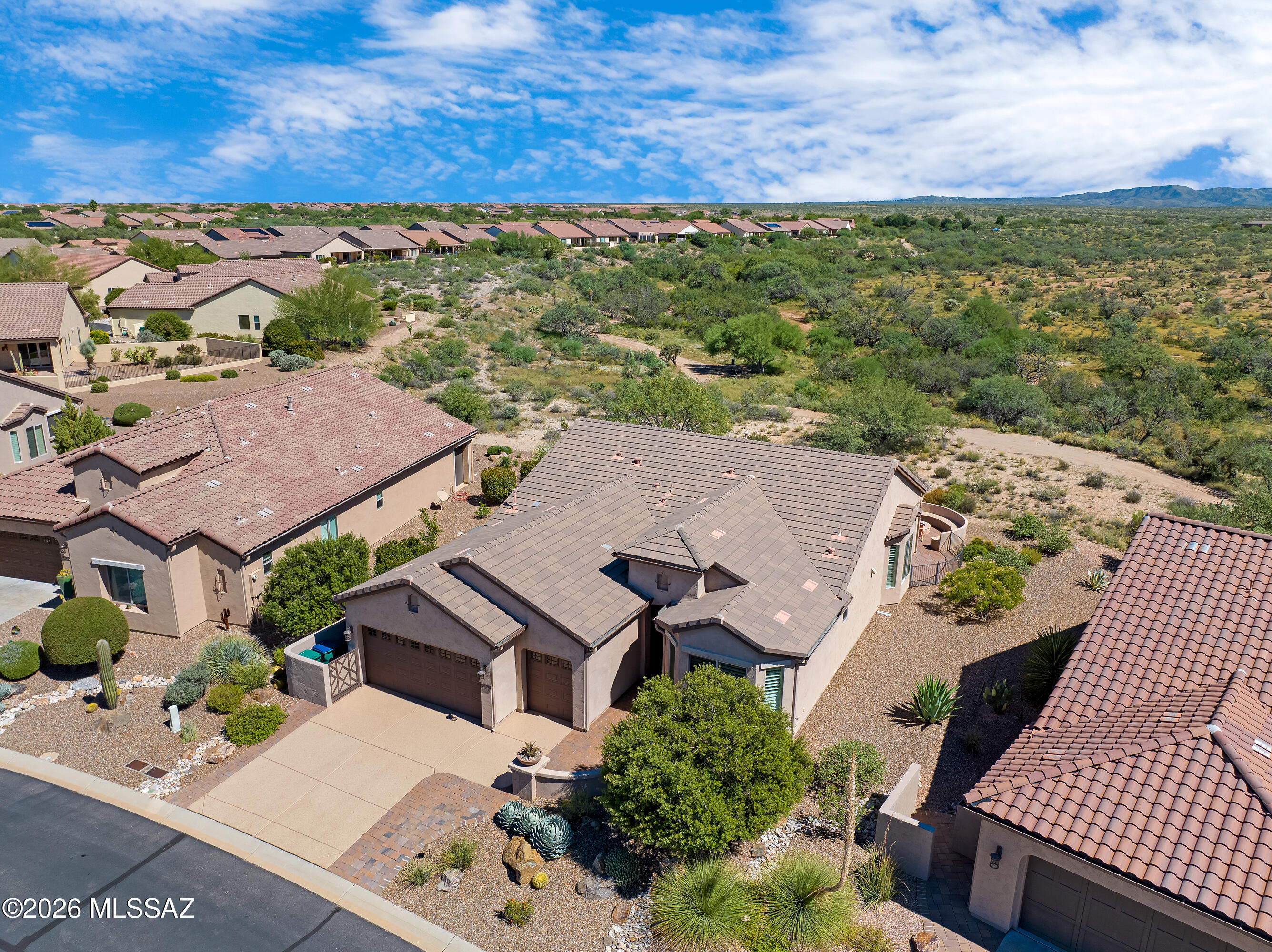 Aerial view of a stucco home with tile roofs, desert landscaping, and surrounding mountain scrub.