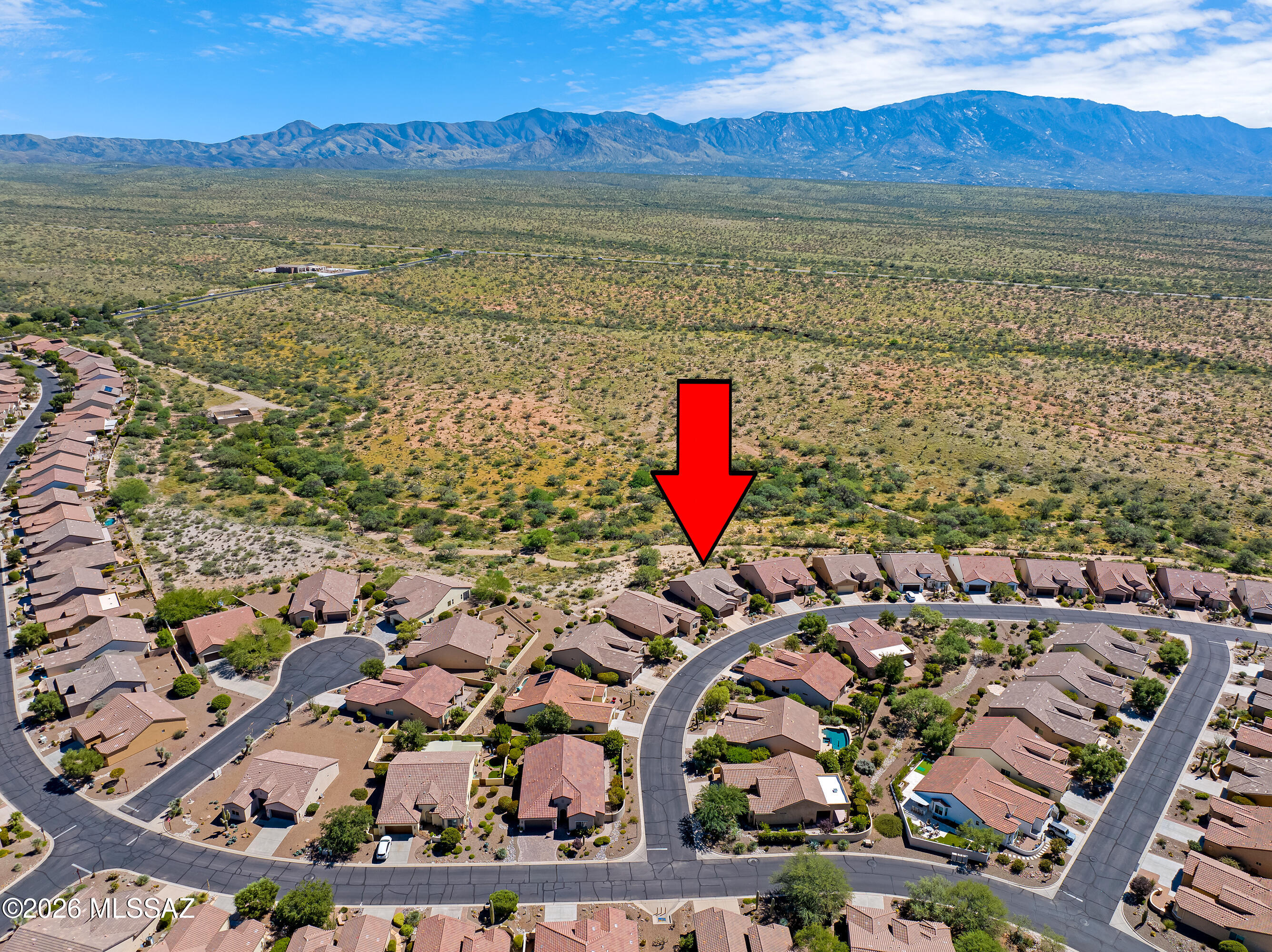 Aerial view of a desert parcel marked by a red arrow, with homes below and mountains in the distance.