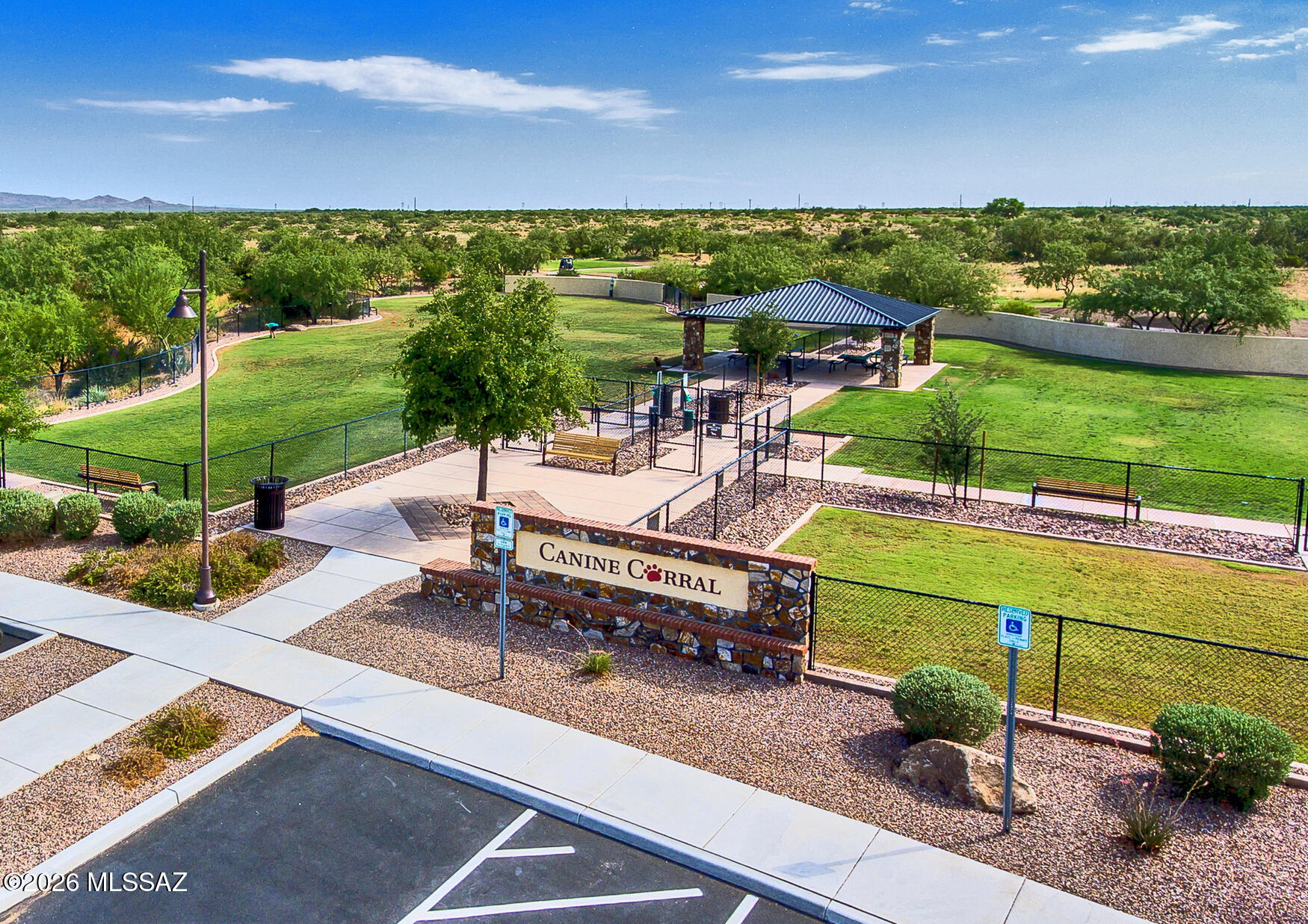 Fenced community dog park with grassy play areas, a shade pavilion, and benches.