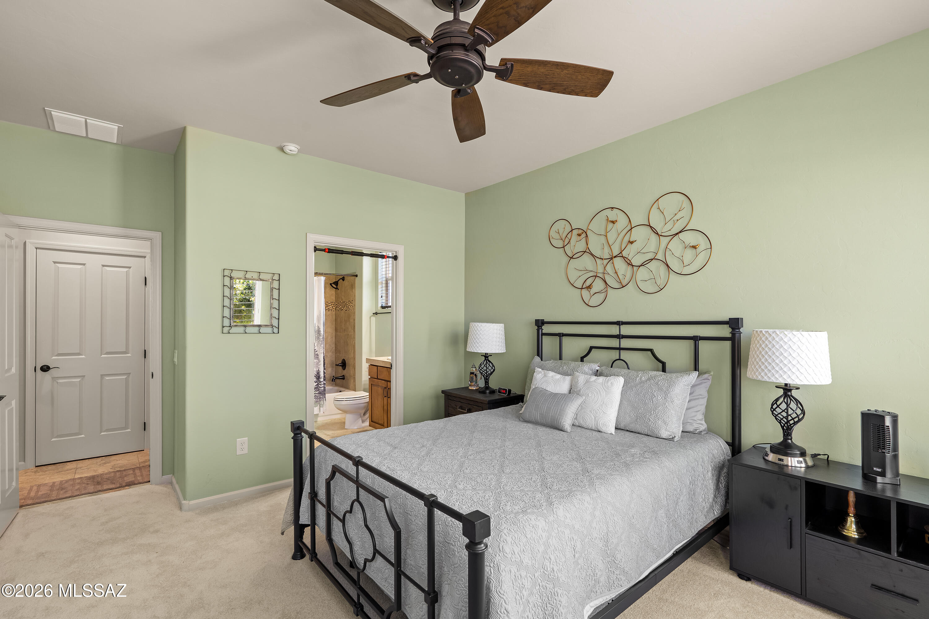 Bedroom with black metal bed, pale green walls, and doorway to ensuite bathroom.