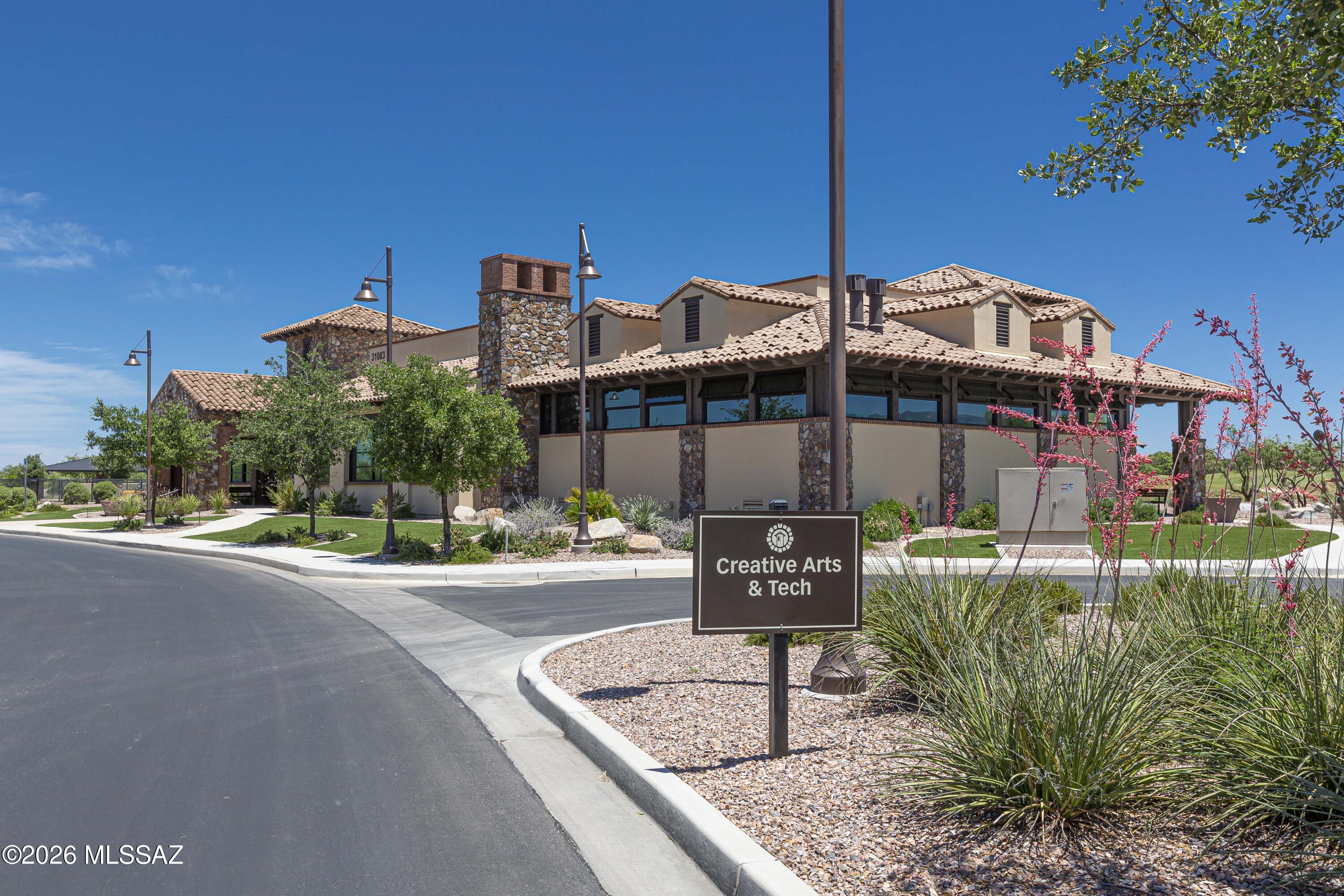 Tan stucco building with stone columns and tiled roof beside a Creative Arts & Tech sign.
