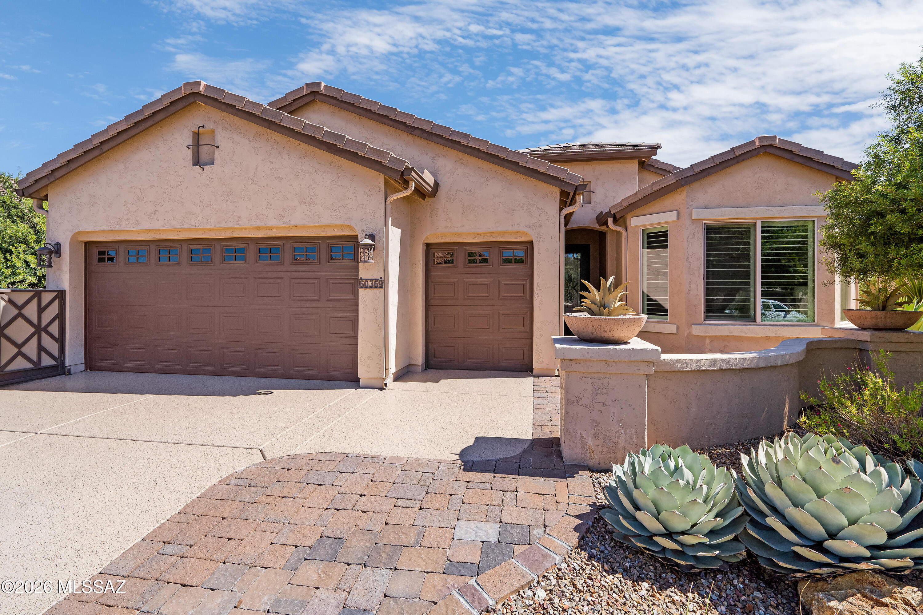 Tan stucco home with two brown garage doors and large agave plants beside the paver walkway.