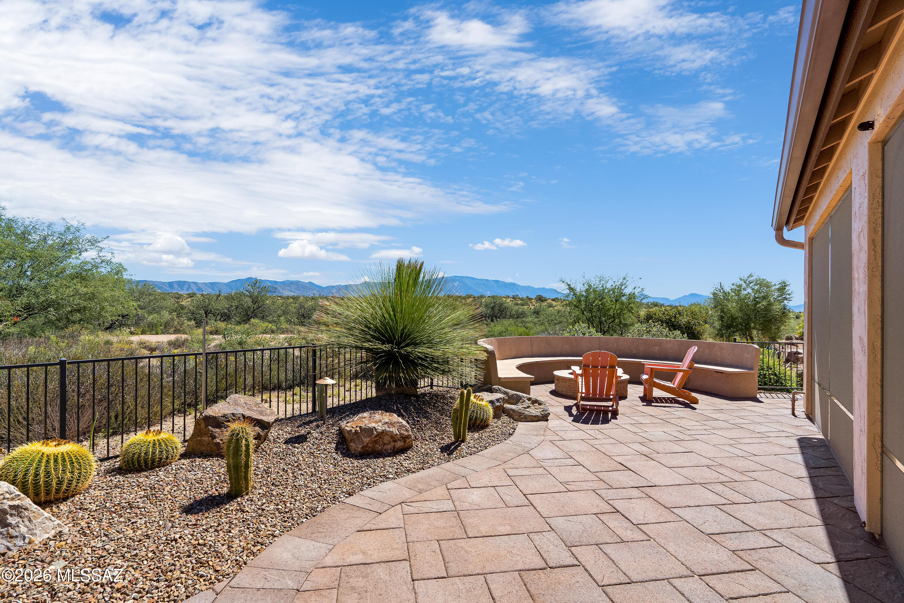 Desert patio with orange Adirondack chairs, a fire pit, cacti, and mountain views.