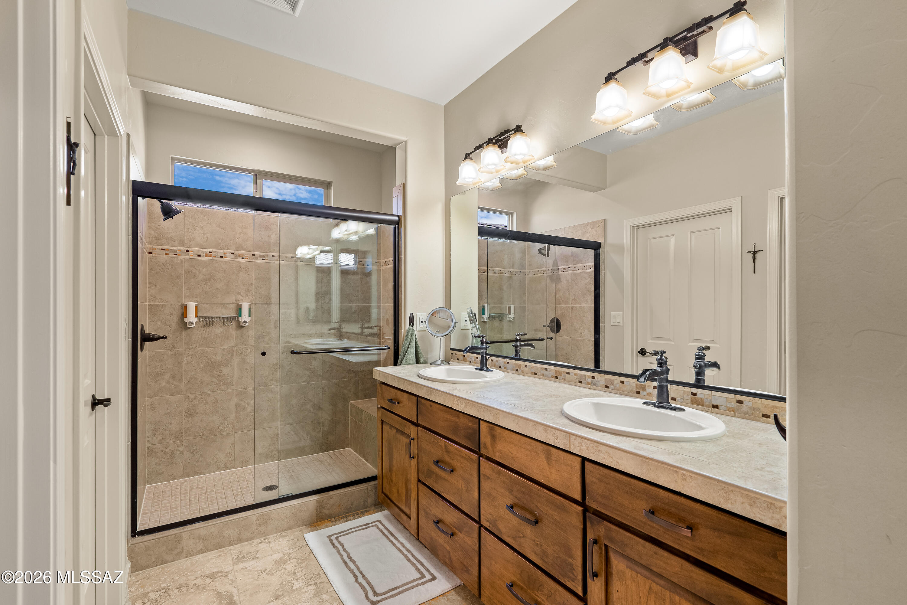 Bathroom with a glass walk-in shower and a long wooden double-sink vanity.