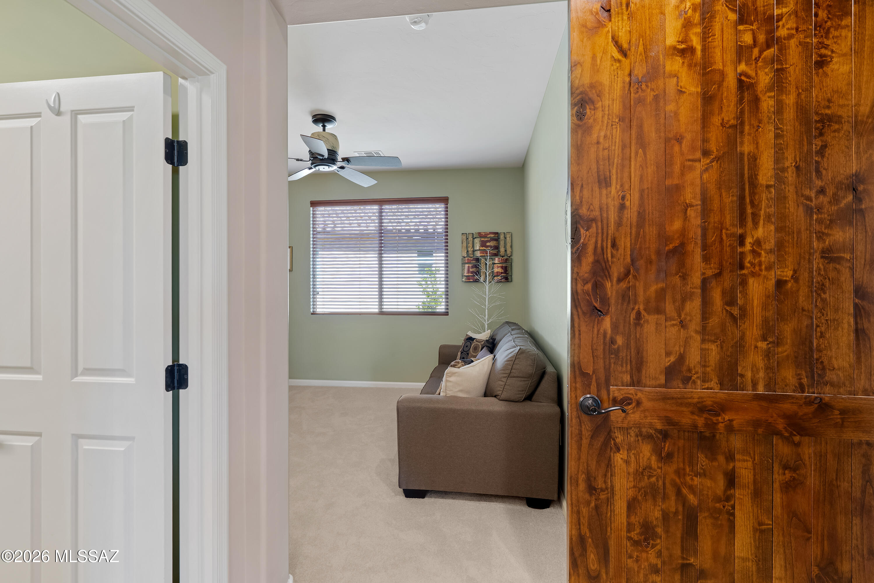 Furnished living room with a brown sofa, window blinds, and rustic wooden door.