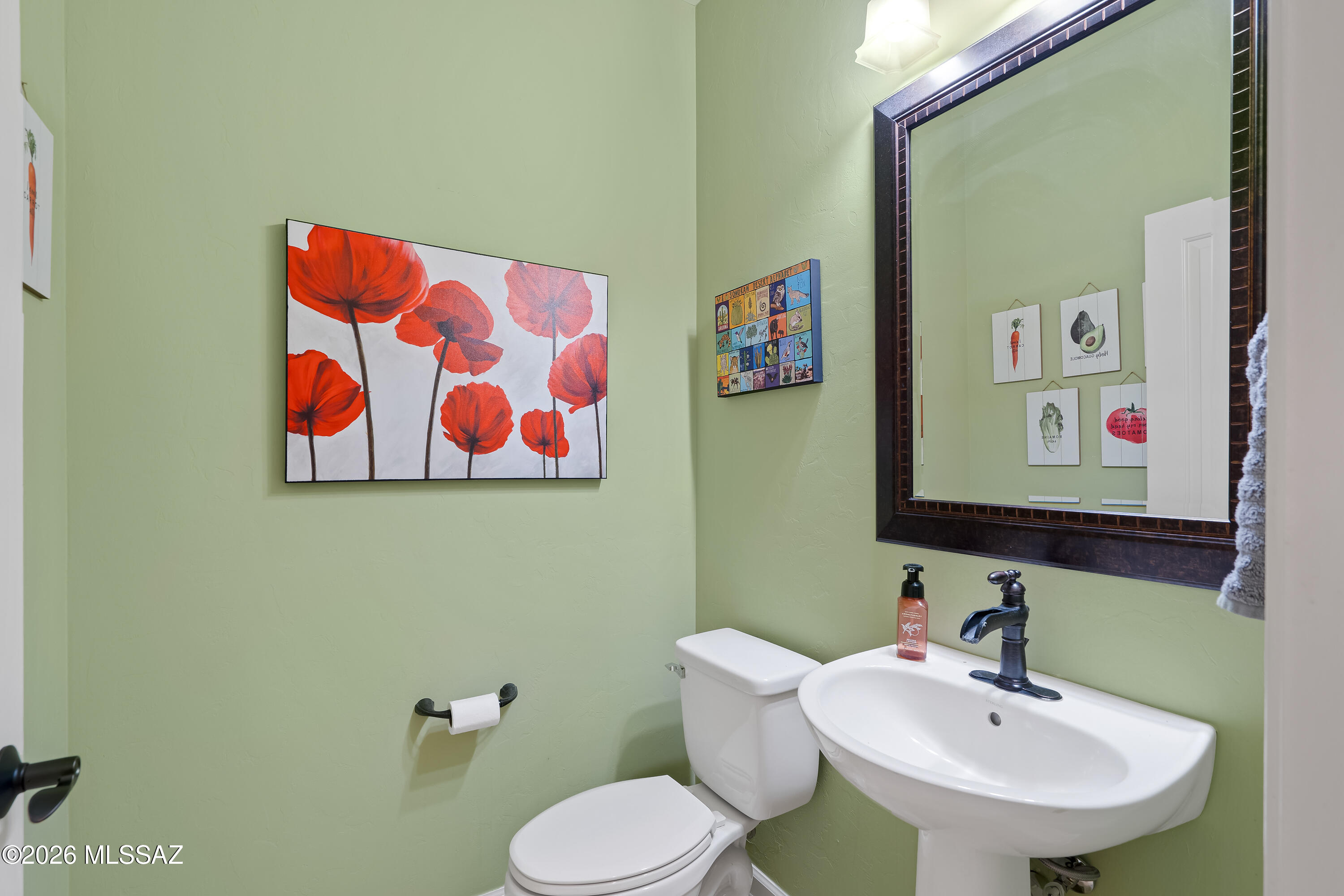 Bathroom with pale green walls, a white pedestal sink, large mirror, and red poppy artwork.