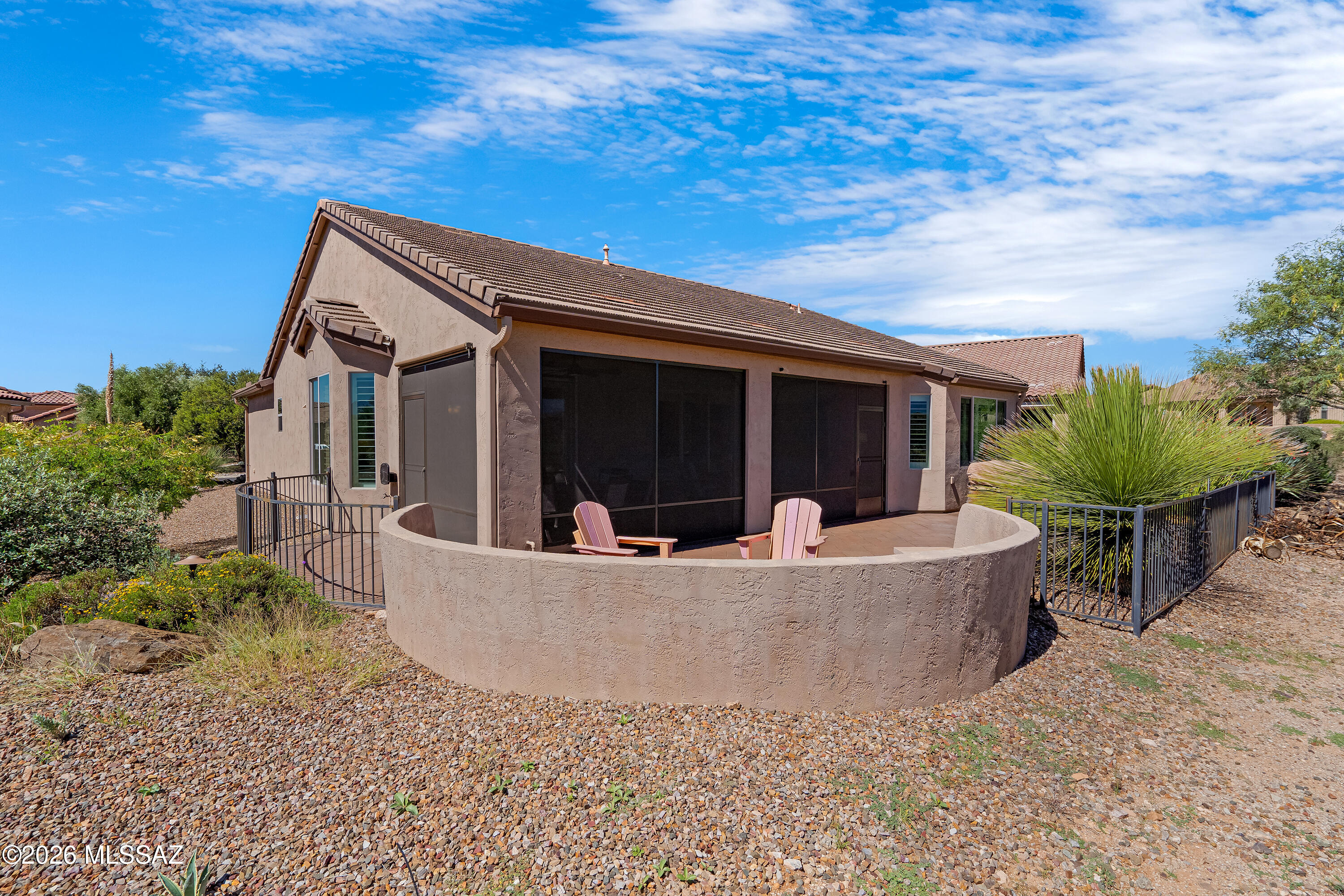 Home’s rear screened patio with pink chairs and gravel desert landscaping.